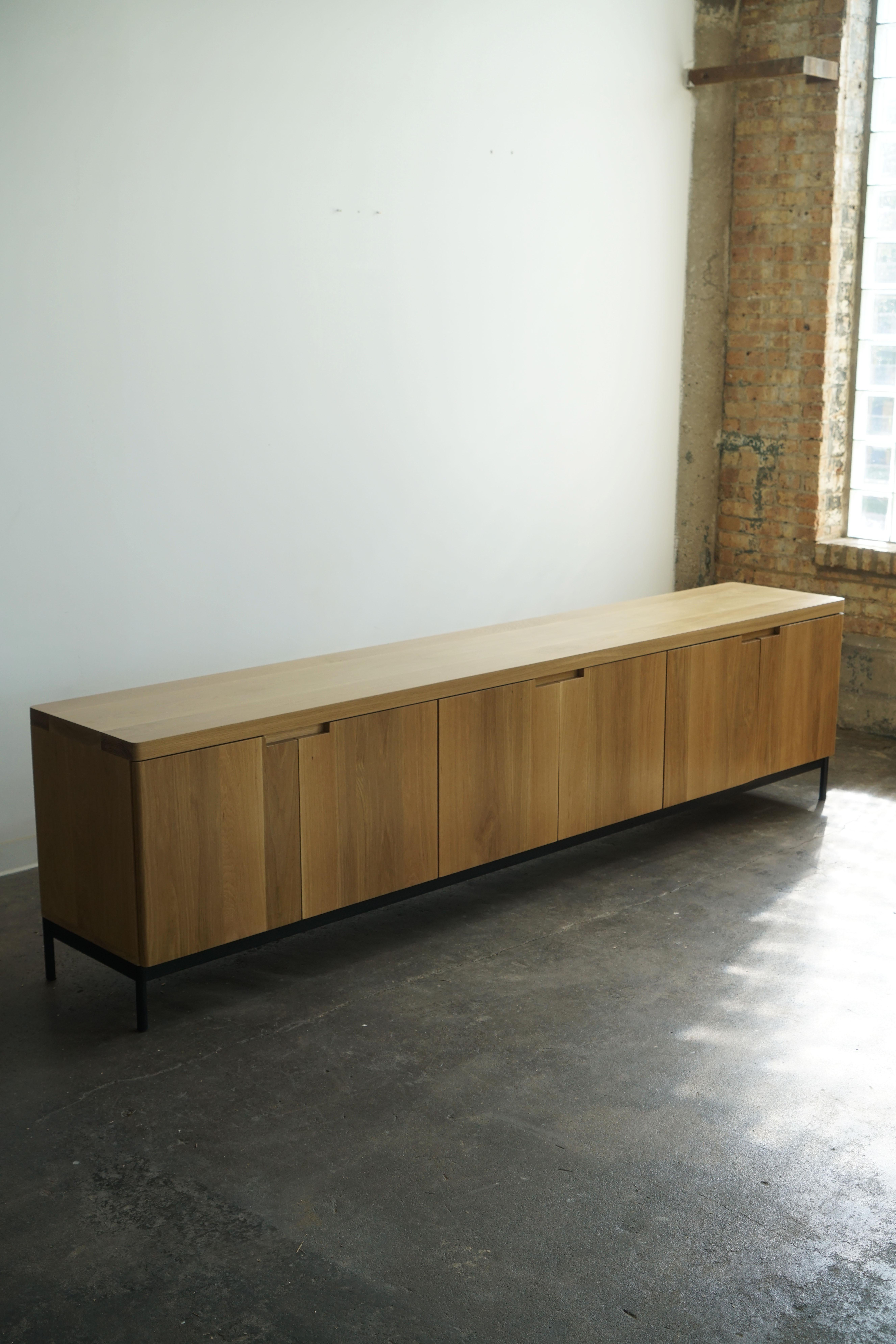 Contemporary solid white oak credenza in a natural finish.
Complete with (6) soft-close doors, adjustable shelves inside, and a steel base. 

Credenza pictured has dimensions of: 108” L x 19” D x 29” H.

This piece is made-to-order, and custom