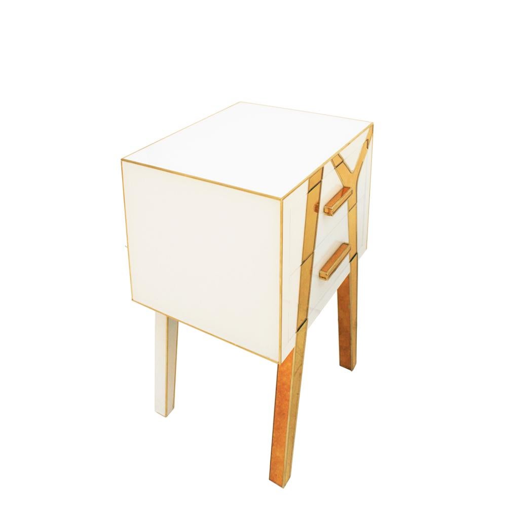 An elegant pair of bedside tables designed and produced by L.A Studio Interiorismo. Structure made of solid wood claded in white and gold glass with brass details. Composed of two drawers and asymmetric legs.
Golden glass color and brass finials