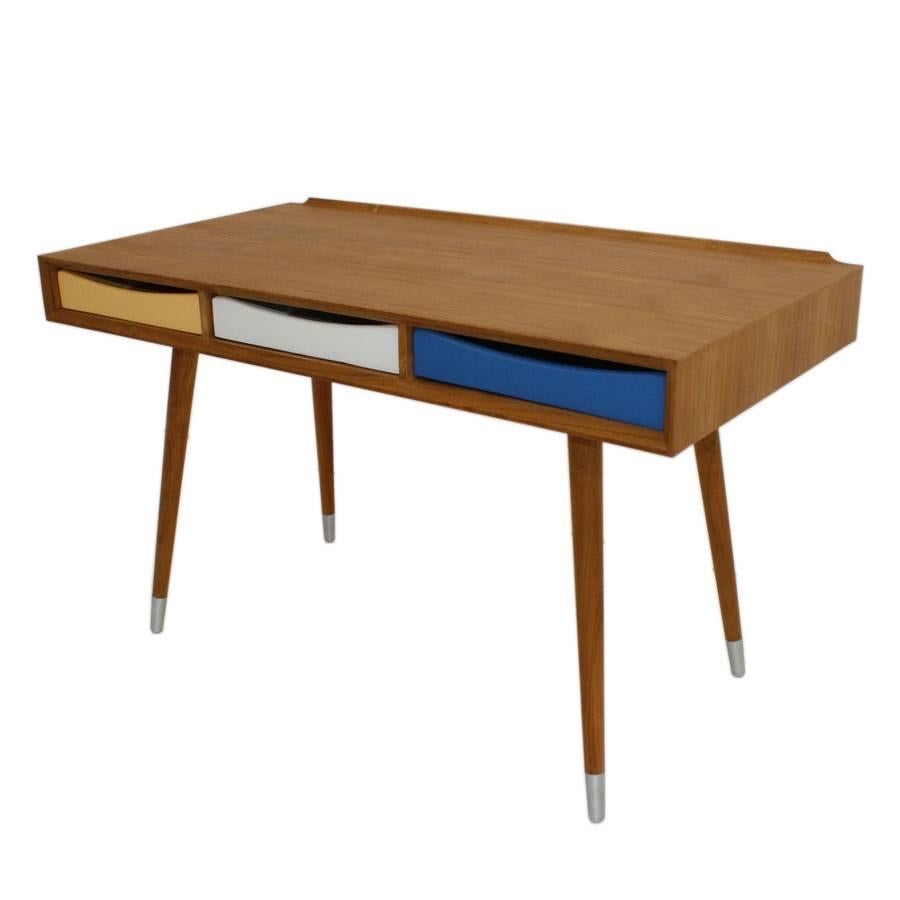 A contemporary birch solid wood desk with three colored lacquered surface drawers and conical legs with metal finials on feet, Italy.