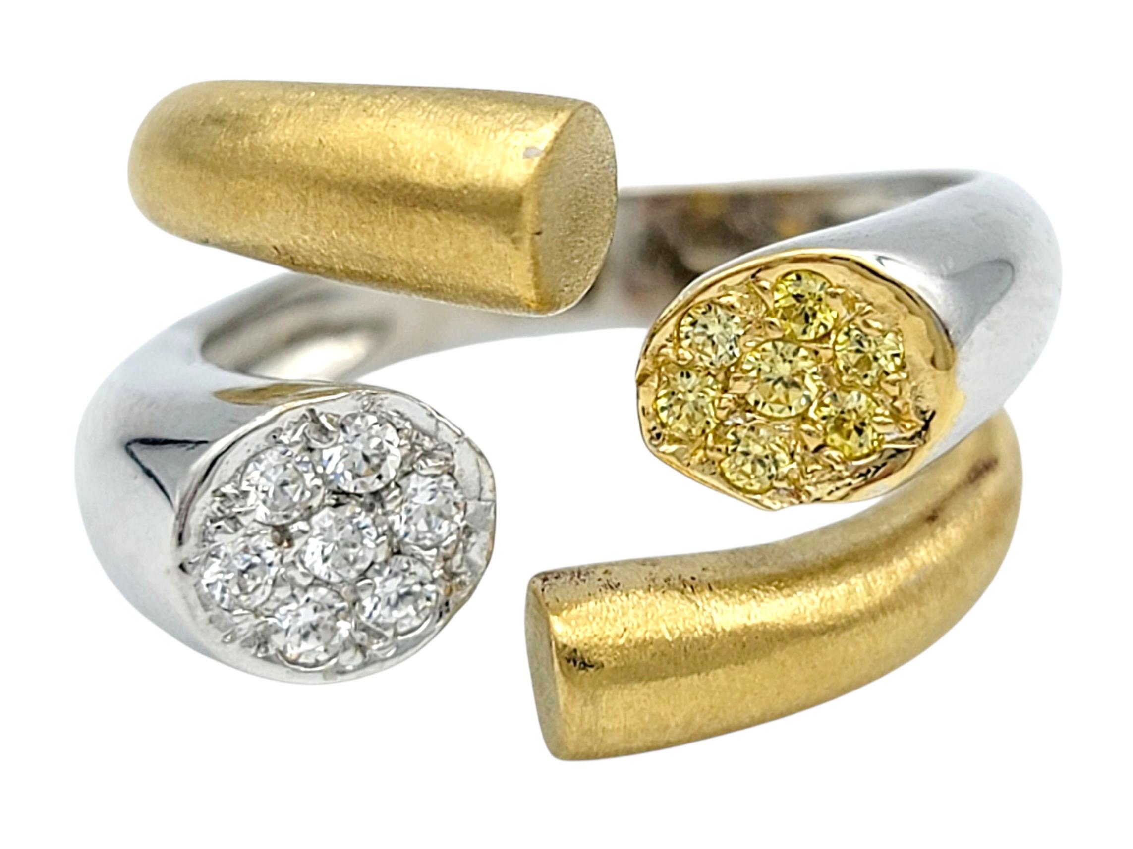 Ring Size: 7.5

This contemporary ring features a striking split shank design that elegantly wraps around the finger. At each end of the bypass style setting, clusters of shimmering diamonds create circular focal points — one gleaming in bright