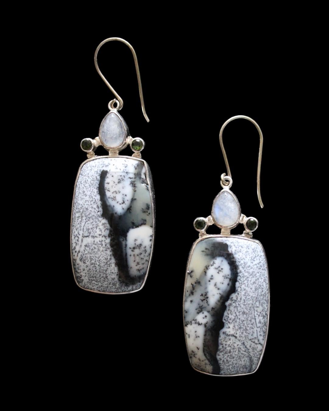 These stunning earrings feature rectangular cut dendritic opal cabochons accented with teardrop moonstones and faceted peridot accent stones. Dendritic opal, also known as dendritic agate, has an opalescent surface and contains small, branching tree