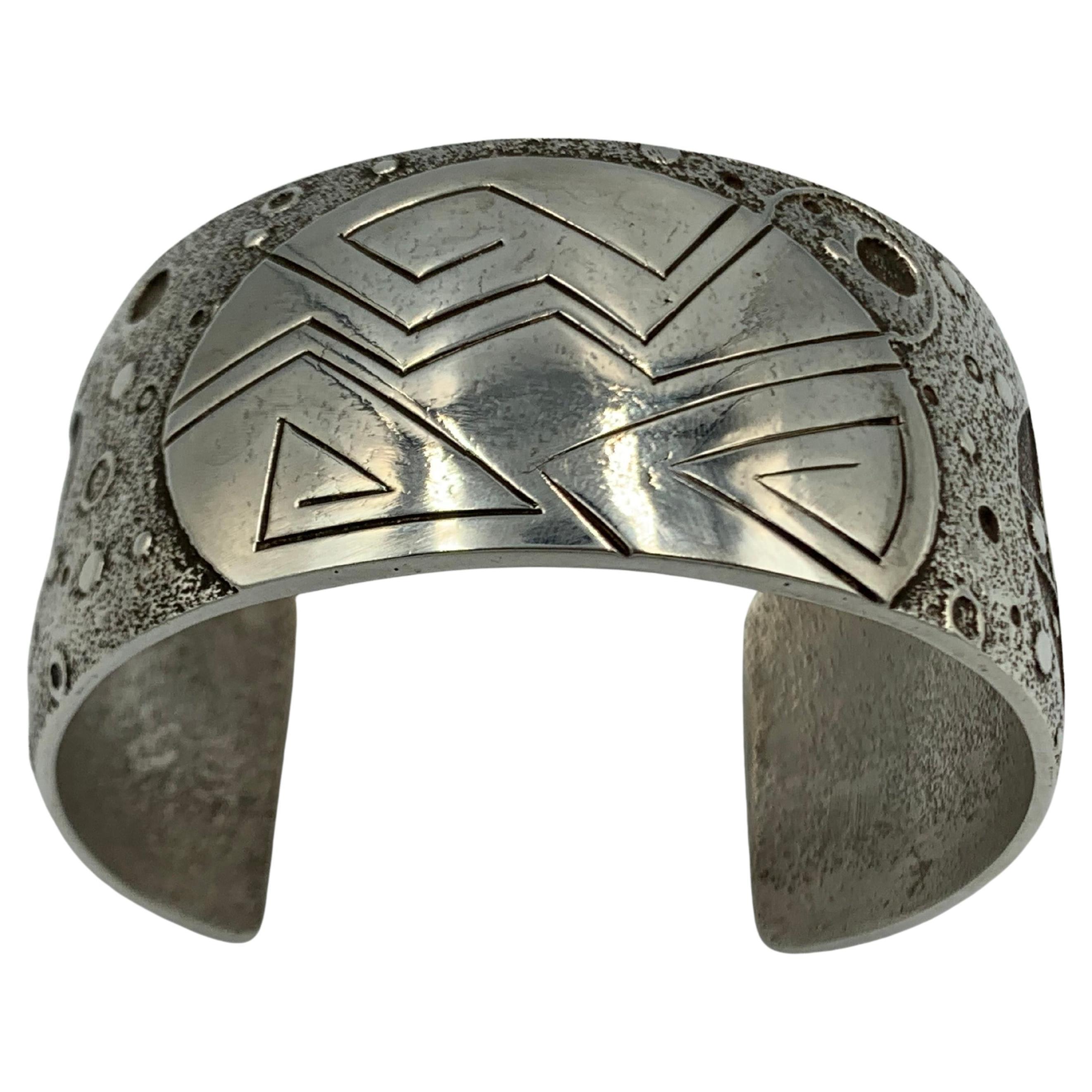 Brazalete de plata de ley fundida en toba del sistema solar, obra del orfebre navajo Fidel Bahe, es un pictórico con lunas, planetas. El puño estampado a mano con textura mide 5 3/4