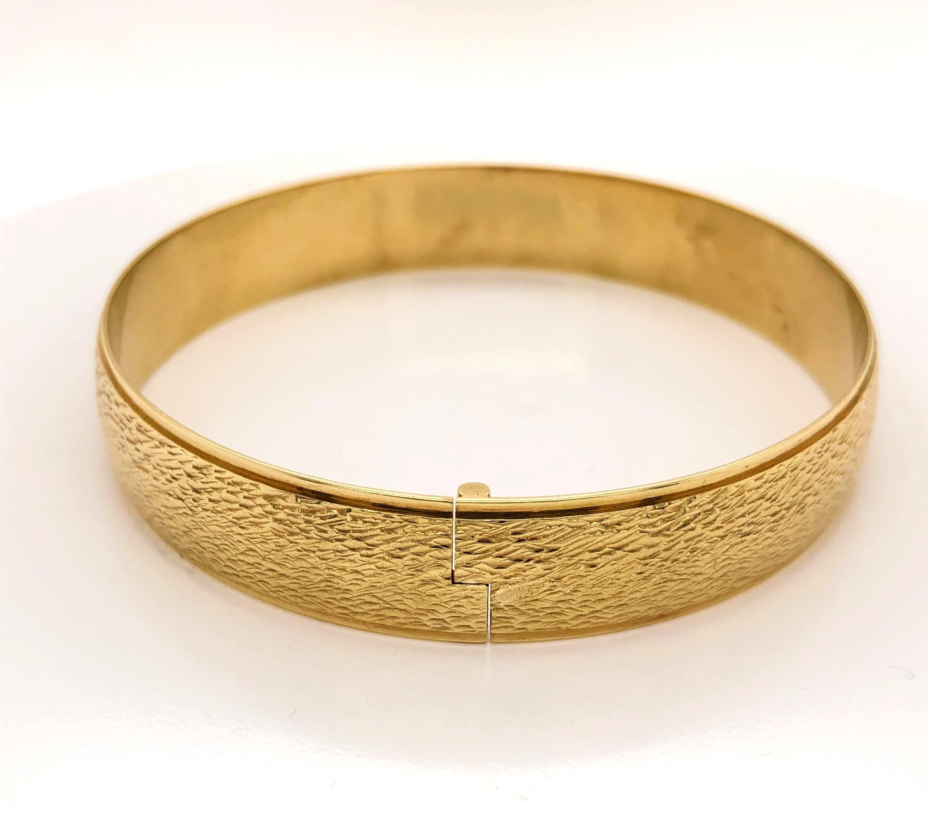 In bright fourteen carat 14K yellow gold, this sleek bangle bracelet displays contemporary styling with its textured finish complemented by a recessed polished edge detail. Quality made with a 
no-show mystery hinge for ease of wear. The bracelet