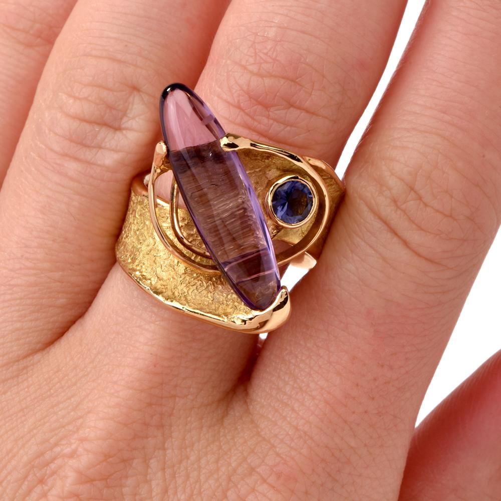 This avant-garde ring of surrealistic inspiration is crafted in 18 karats matted textured and polished yellow gold and weighs 18.9 grams. The ring exposes a long oval cabochon amethyst of 4.50 carats mounted in diagonal position adjacent to a
