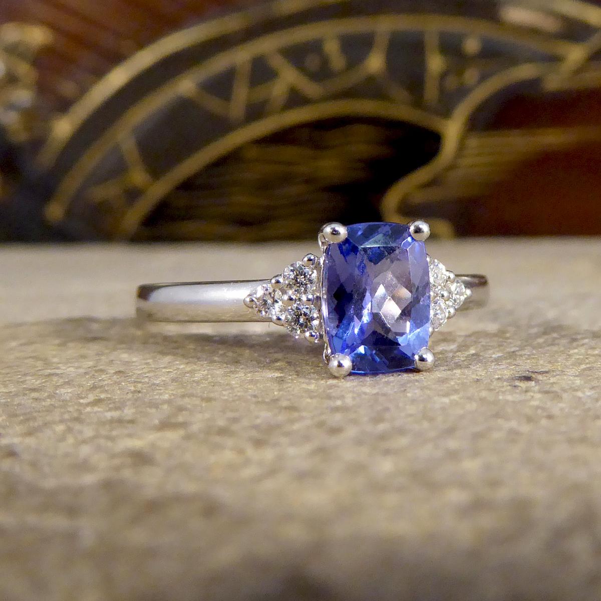 A very elegant ring that is holds a beautiful blue Cushion Cut Tanzanite in the centre that almost shows flashed of slight purple in different lights, such a gorgeous coloured stone. Either side of the gemstone sit three bright and clear round cut