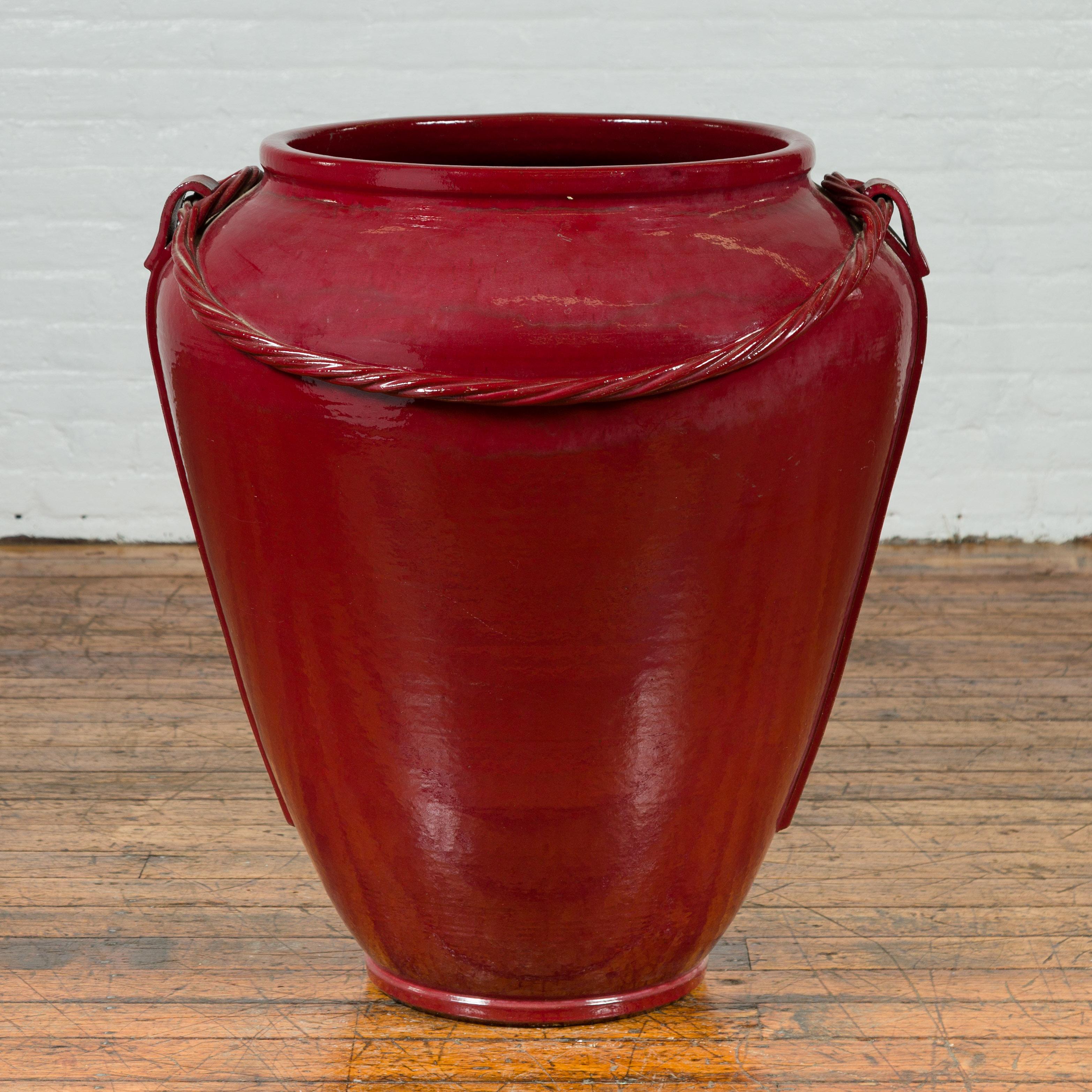 A contemporary Thai oversized oxblood water jar from Chiang Mai with rope design. Created in Northern Thailand, this extra-large water jar features a deep oxblood finish and lateral handles securing a twisted rope design. With its clean lines and