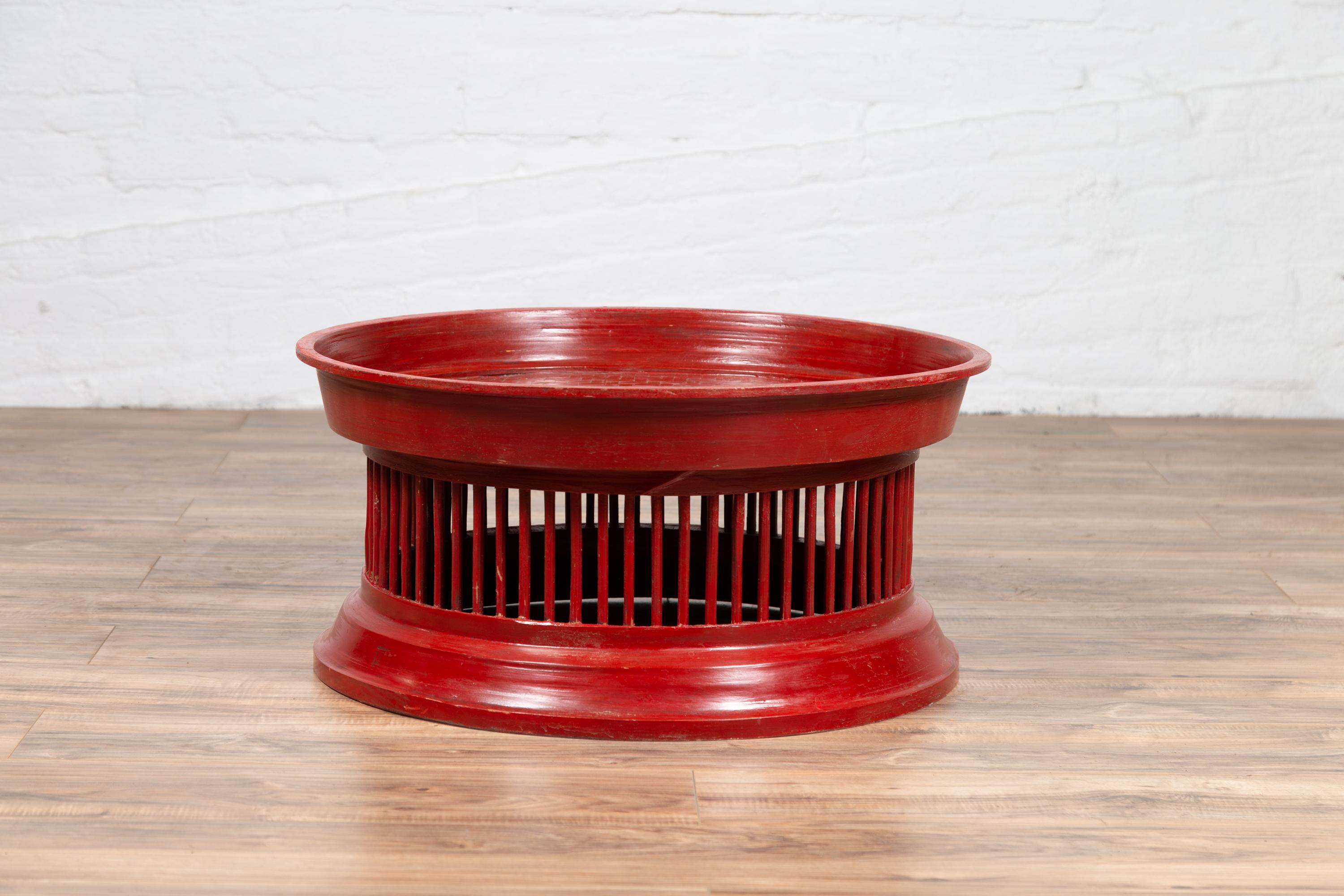 A Thai contemporary rattan drum coffee table with red lacquer, inspired by an antique tribal tray. This Thai coffee table features a drum shape, presenting a circular tray top sitting above a body rhythmically accented with spindle motifs, the