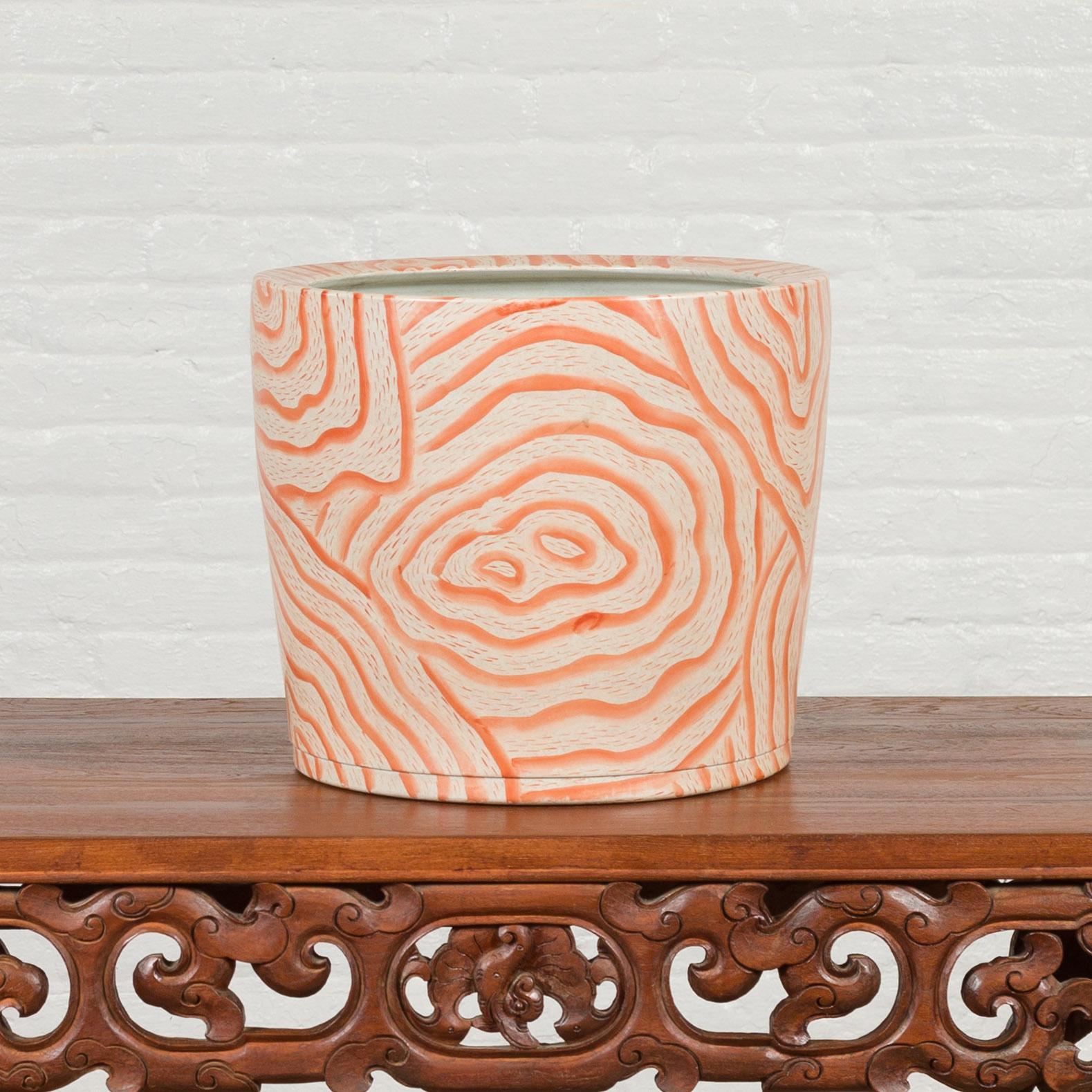 A contemporary Thai salmon colored flower vase with stripes. Crafted in Thailand, this vase features a simple silhouette adorned with a salmon colored decor made of various stripes imitating a cut wood grain. With its sleek lines and subtle colors,