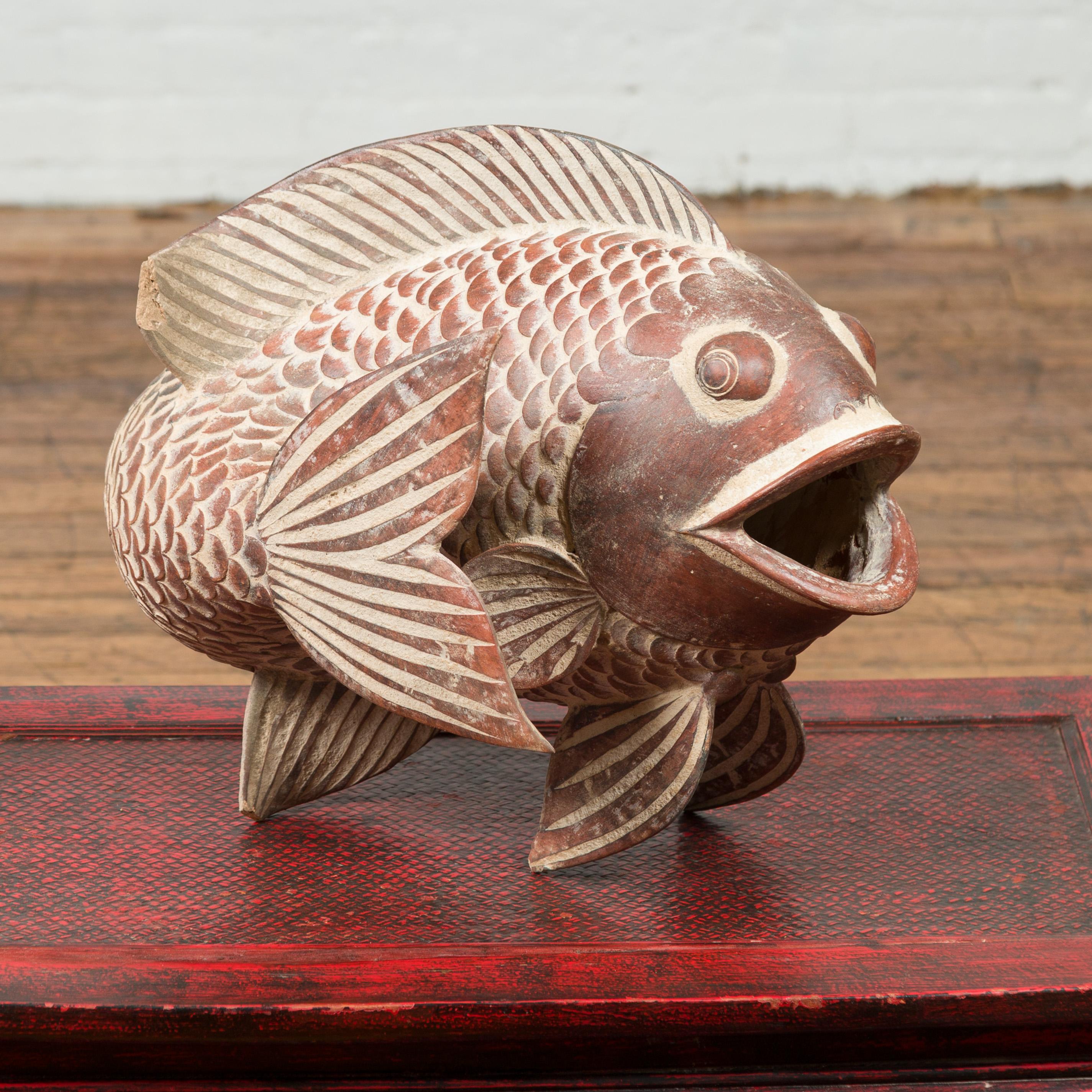 A contemporary Thai terracotta fish sculpture with brown accents and nice detailing. Crafted in Thailand, this contemporary terracotta fish will make for a charming garden ornament. Its tail fin showing a graceful forward movement, the fish opens