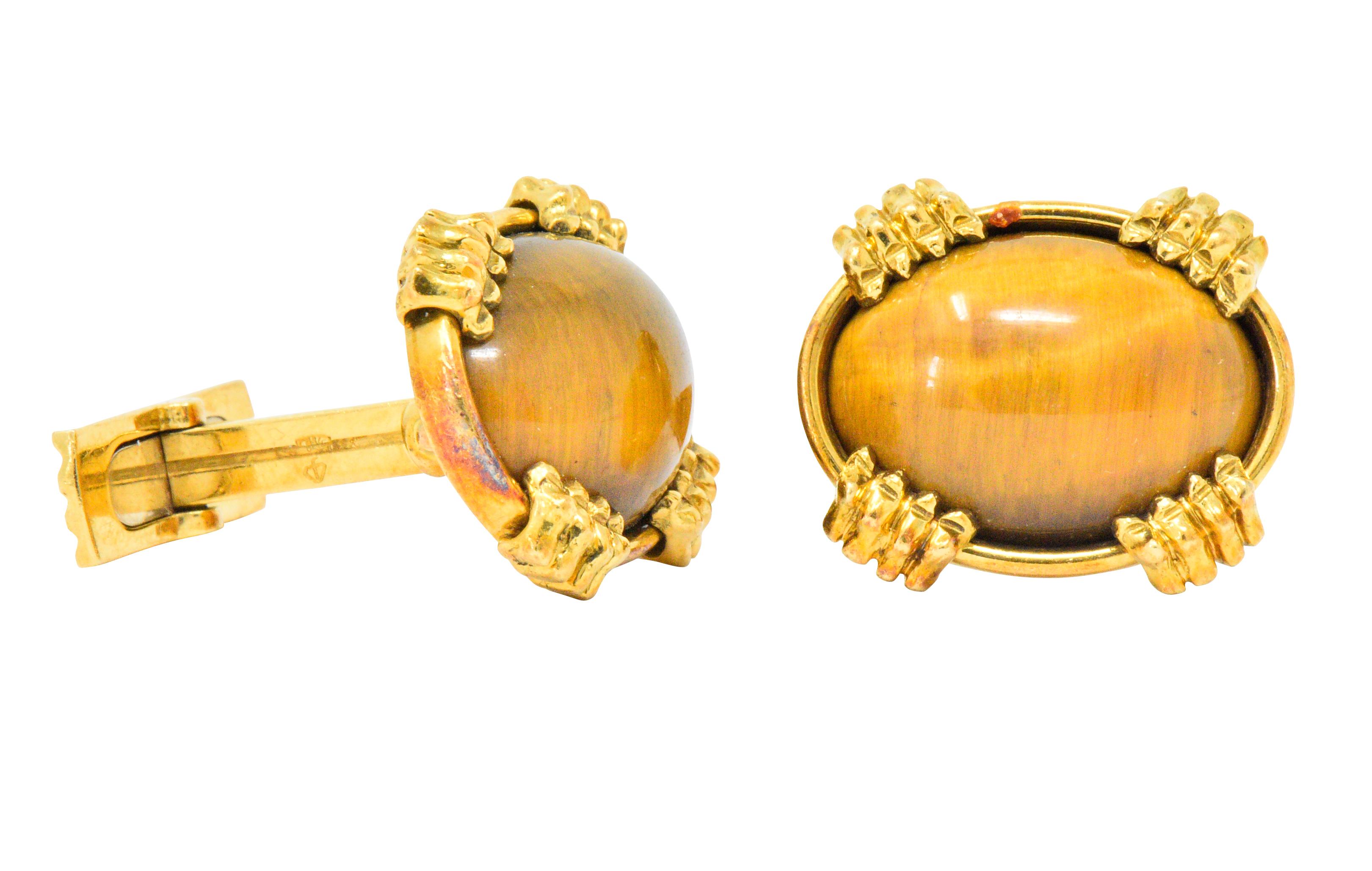 Lever style cufflinks featuring oval tiger's eye cabochon, measuring approximately 17.8 x 13.6 mm

Opaque and a well-matched gold to brown color with moderate chatoyancy

Bezel set in a polished gold surround with four stylized claw accents 

With