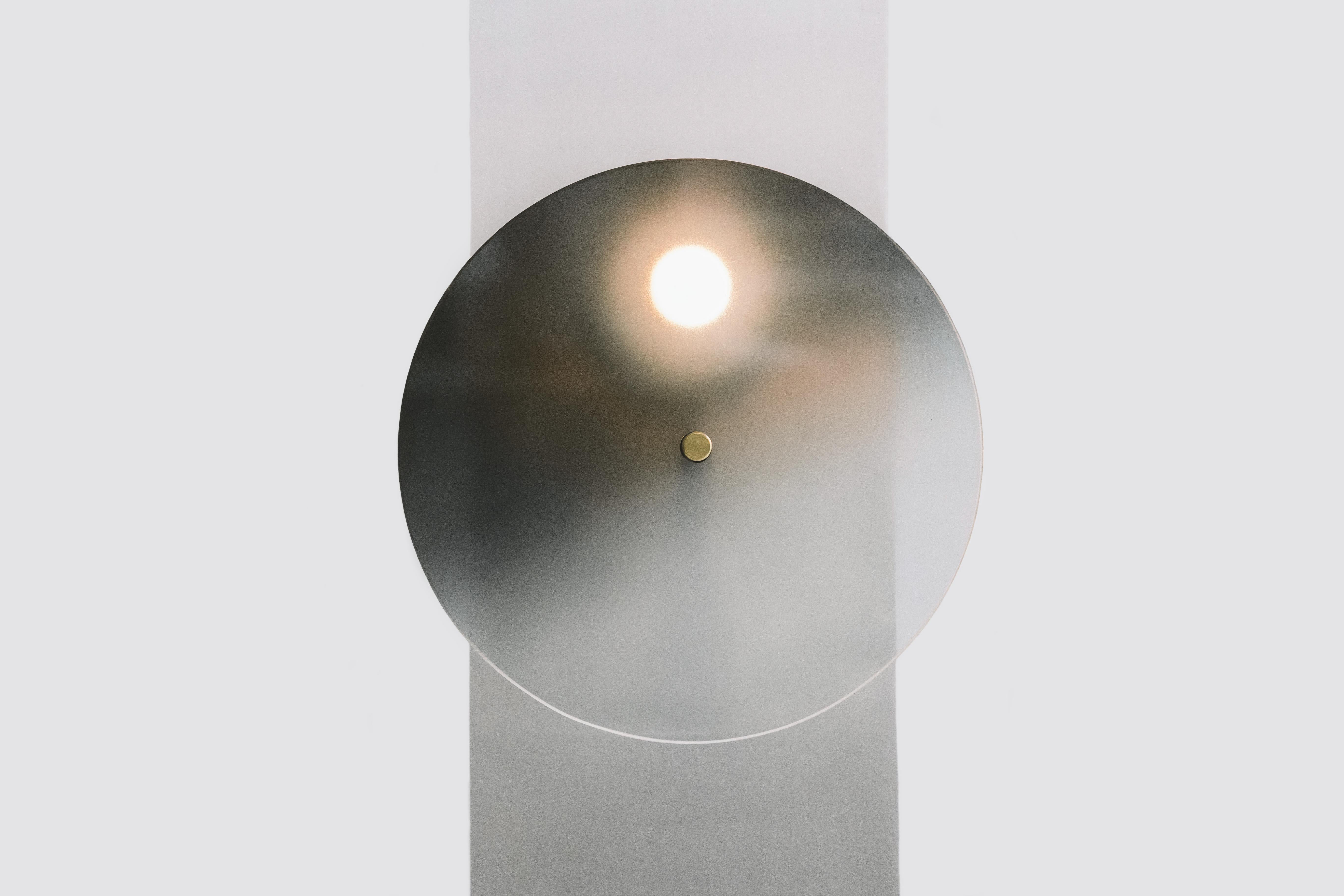 Inherent in its design, the Tinge series draws the user to the source of light. The brass knob controls the position of the tinted glass disc, which, when spun, manually changes the brightness of light. The analog lighting experience of the Tinge