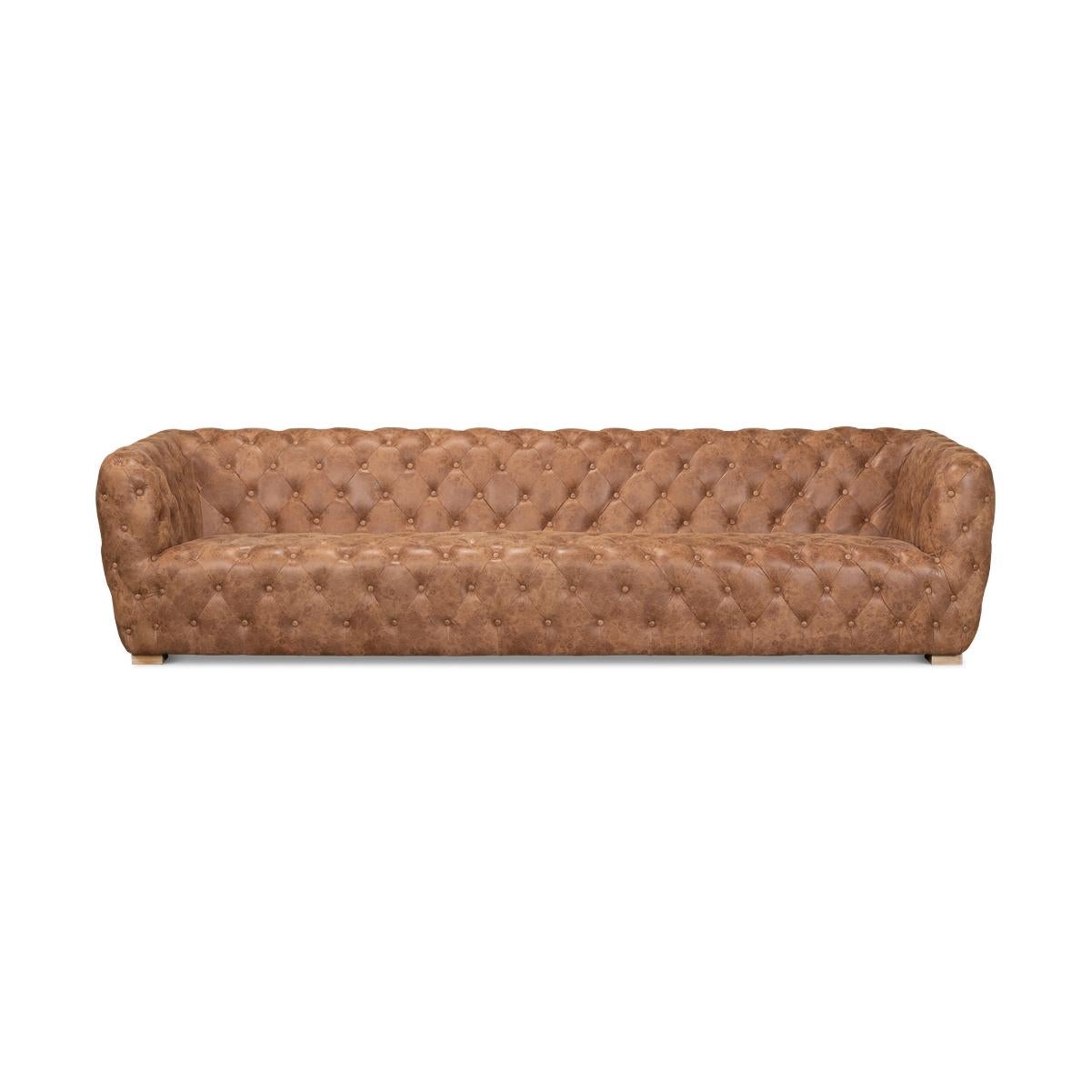 A contemporary-style tufted leather sofa with uniform back and arm height. This sofa has a generous long length and is tufted on its interior and exterior including back and sides. It is upholstered in transitional tan leather color and rests on