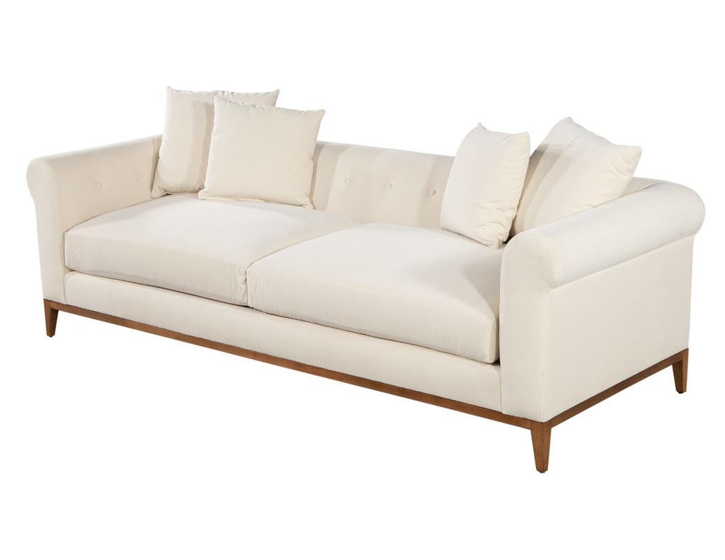 Contemporary tufted sofa with curved arms by Ellen Degeneres Pales Sofa. Beautiful tufted seat back with curved contemporary design. Completed with a simplistic light brown maple frame. Upholstered in a soft light beige fabric. 4 small accent