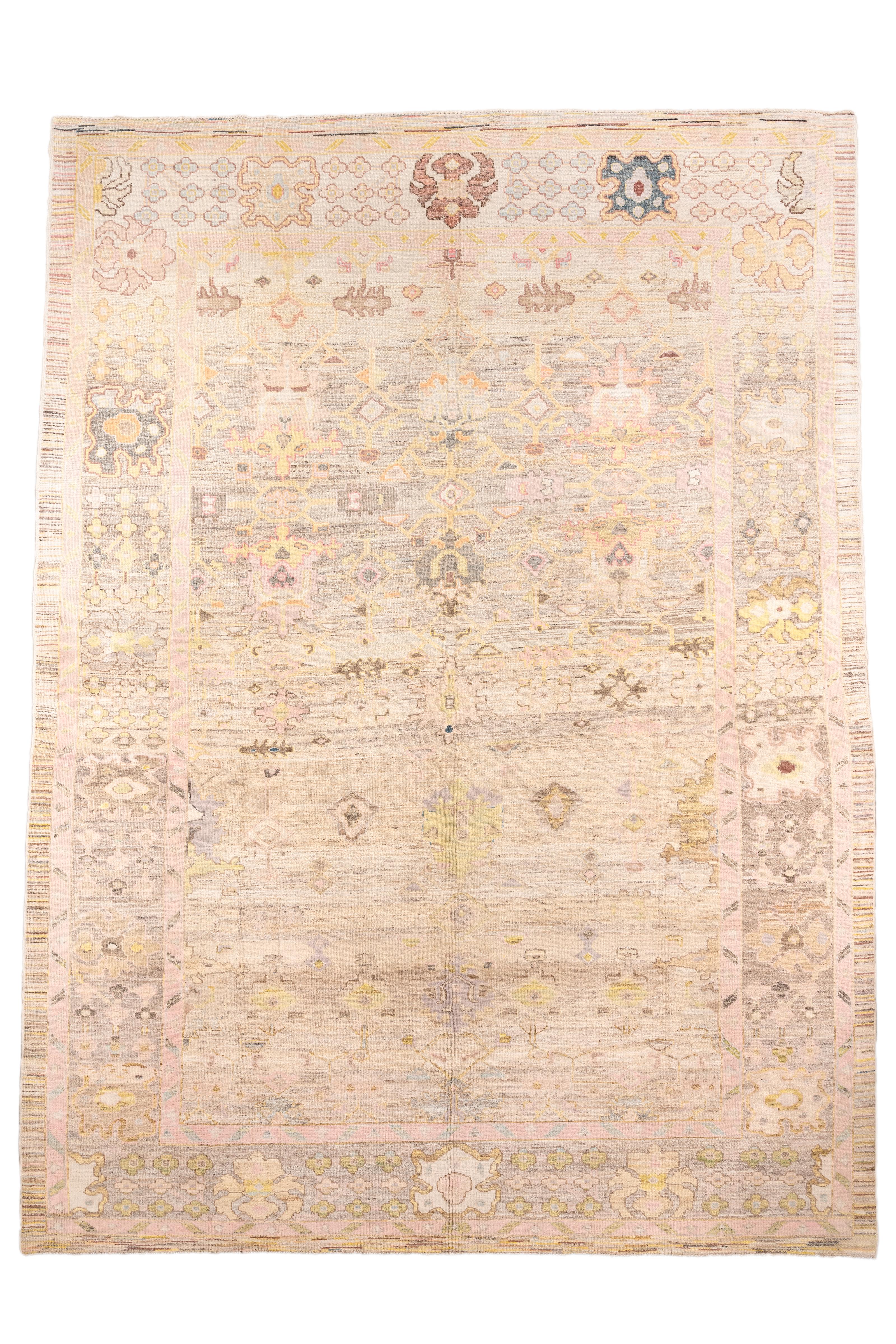  Un tapis turc Oushak raffiné, tissé dans une palette douce et lumineuse d'ivoire, de rose blush, de jaune pâle, de lavande atténuée et de taupe doux. Le champ se caractérise par un design ouvert et aéré avec des médaillons géométriques stylisés et