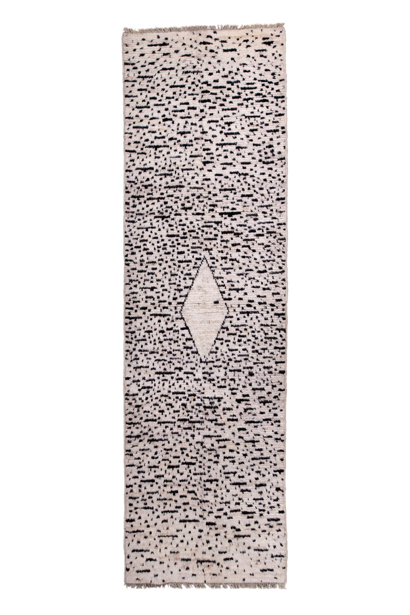 Questo runner Tulu contemporaneo presenta un campo morbido color avorio con un motivo irregolare a macchie e un unico motivo centrale a rombi. La lana a pelo lungo e il design minimalista le conferiscono un aspetto caldo, organico e moderno.