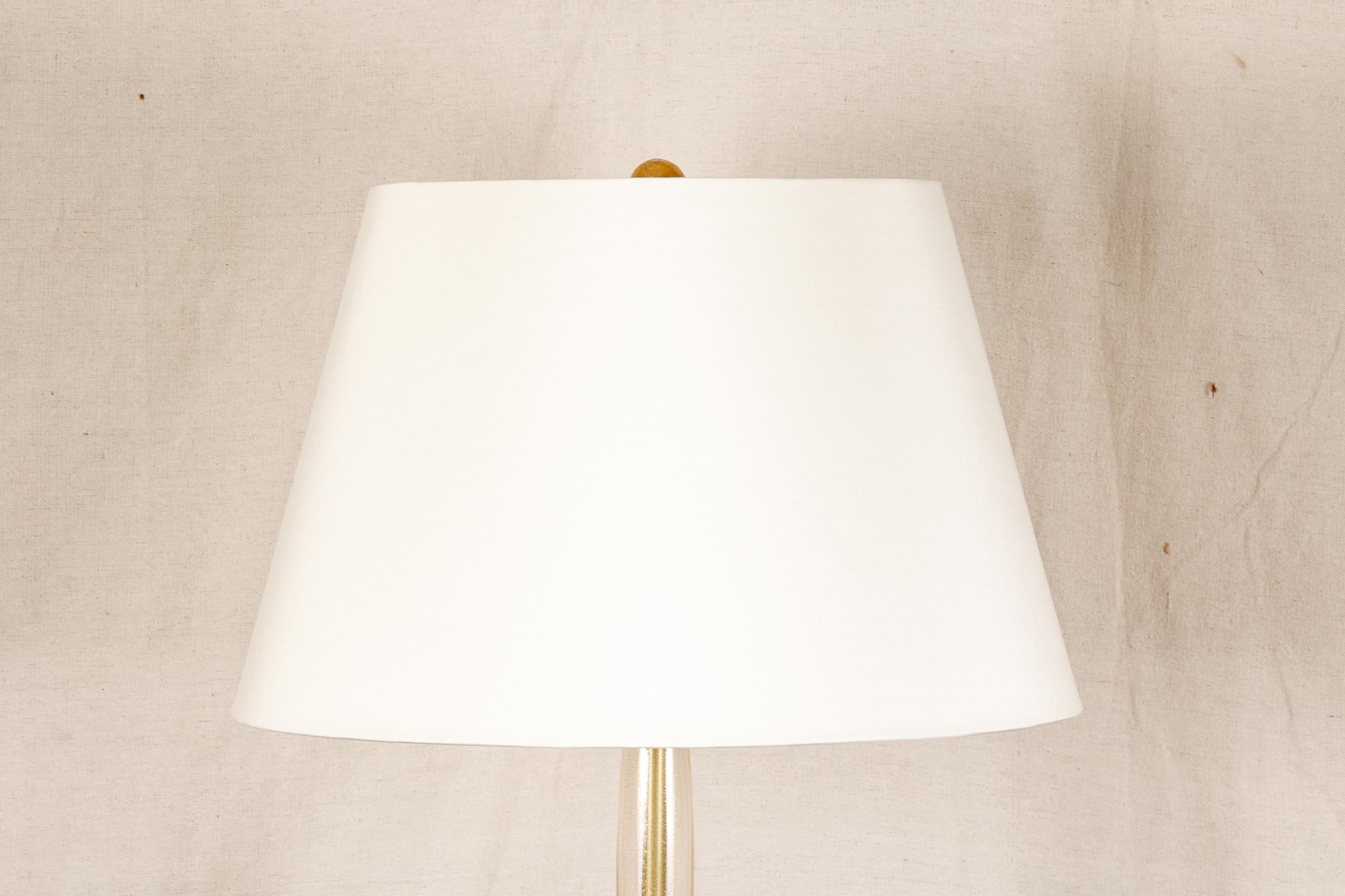 Contemporary twin light gilt Murano glass floor lamp, segmented gilt Murano glass standard with rings and a gilt interior shaft, a round base and ball finial. Twin lights with a white fabric shade. 

Condition: In good, gently used condition.