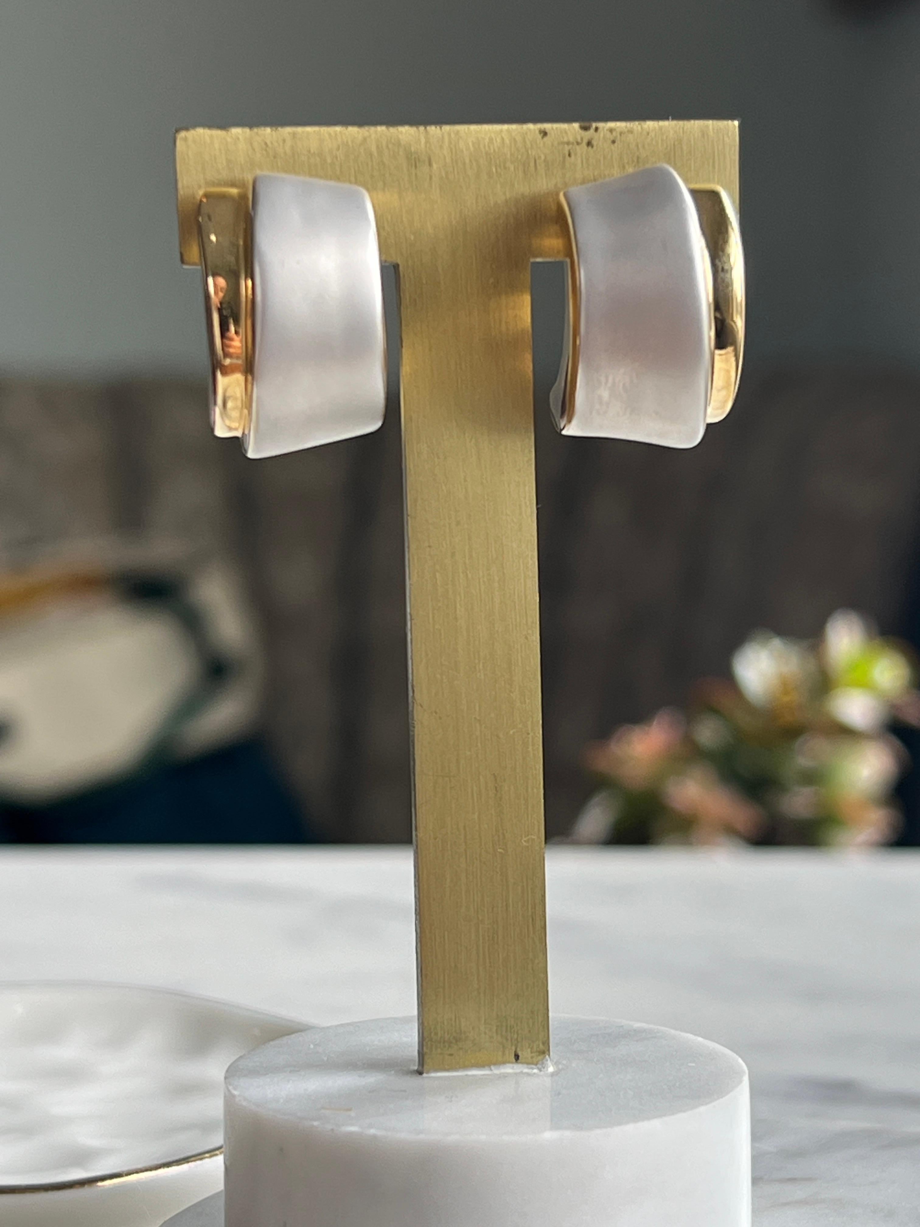 Un par de pendientes contemporáneos de media luna, elaborados con maestría en oro amarillo y blanco de 10 quilates. Con un sofisticado baño de rodio satinado, estos pendientes ofrecen un contraste elegante y moderno que realza su escultural silueta.