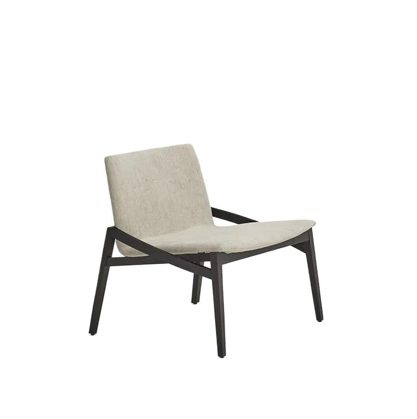 This collection showcases a comfortable lounge chair and footrest upholstered in a luxurious fabric and featuring a sleek beech wood base. The chair's design is both light and inviting, with the slender seat seemingly floating above the frame for a