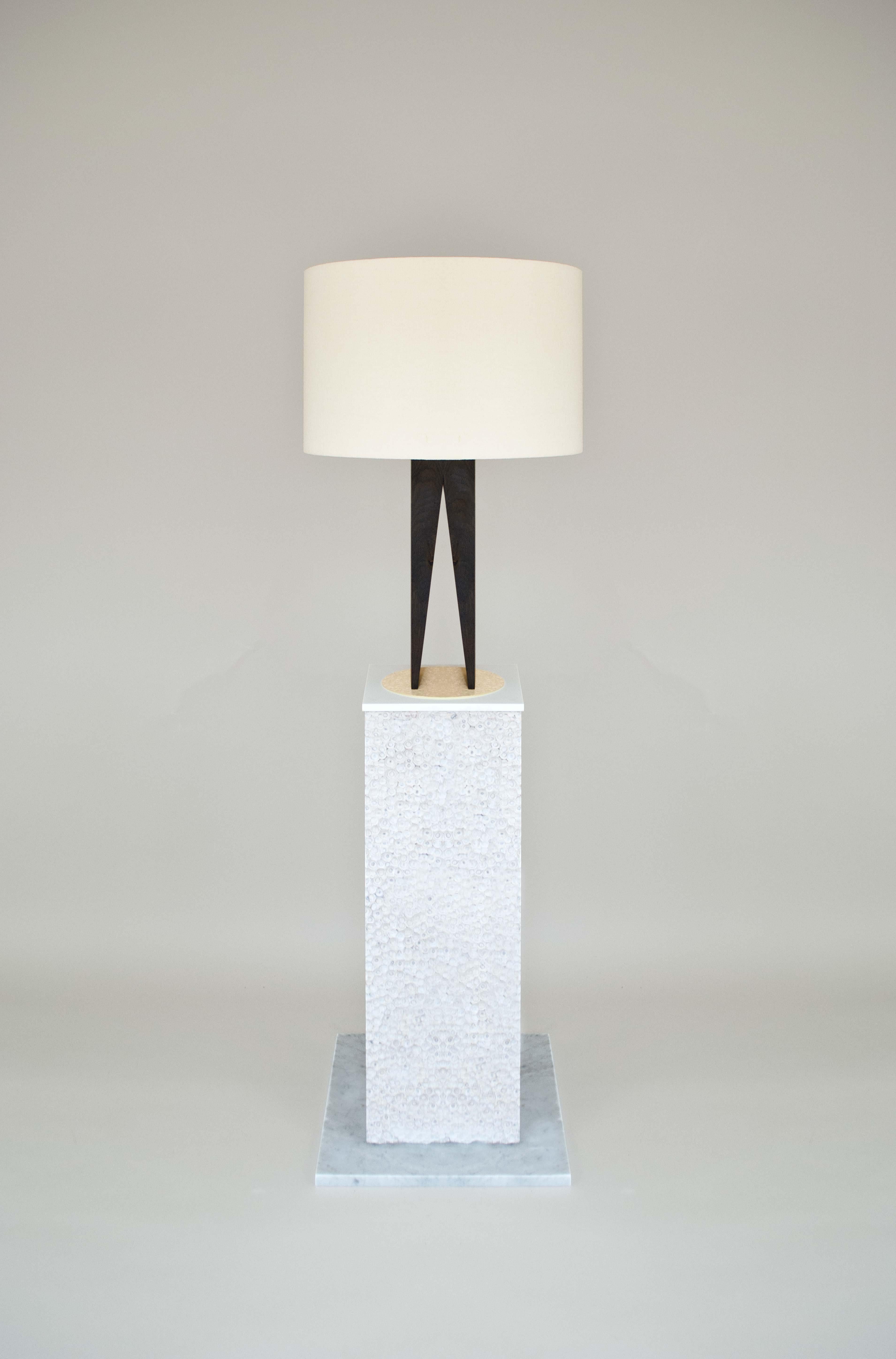 Die von Bauhaus und Art Deco inspirierte V-Lampe besteht aus einem ebonisierten Ständer aus massivem Eichenholz, der auf einer Messinggrundplatte steht. Der Schirm ist aus einem grob strukturierten Leinen aus Italien gefertigt. 

Die Leuchte „V“