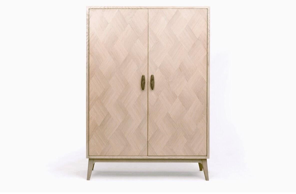 The contemporary cabinet features an intricate marquetry inlay along with bronze handles fashioned after wheat branches. Marquetry, an ancient artistic technique, involves layering veneers to form organic motifs, reflecting traditional
