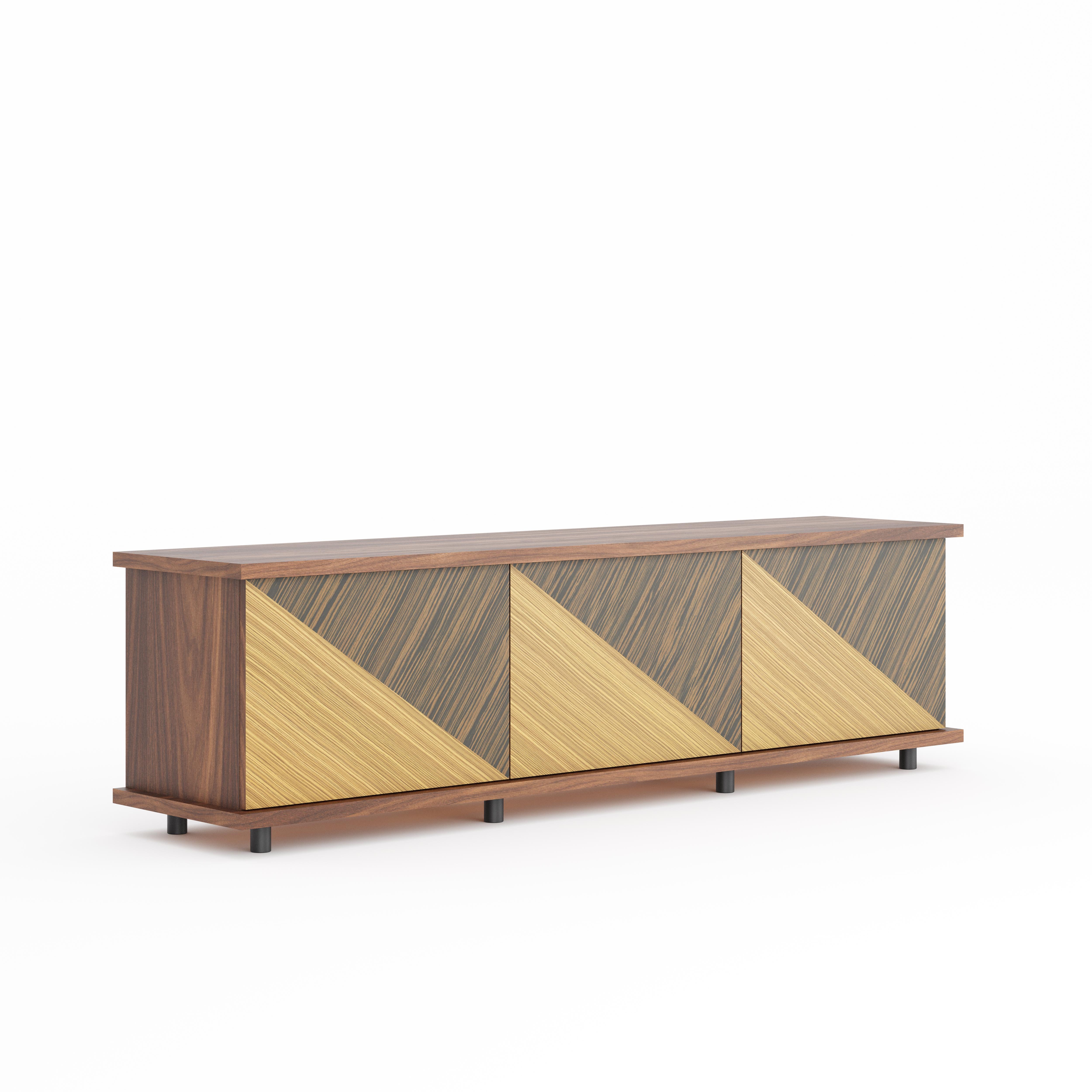 Questa pregiata credenza in noce lavorata a mano presenta un sofisticato equilibrio tra artigianato senza tempo e un audace design contemporaneo.
Il mobile è rivestito in impiallacciatura di noce americano, mentre le tre ante presentano dei frontali