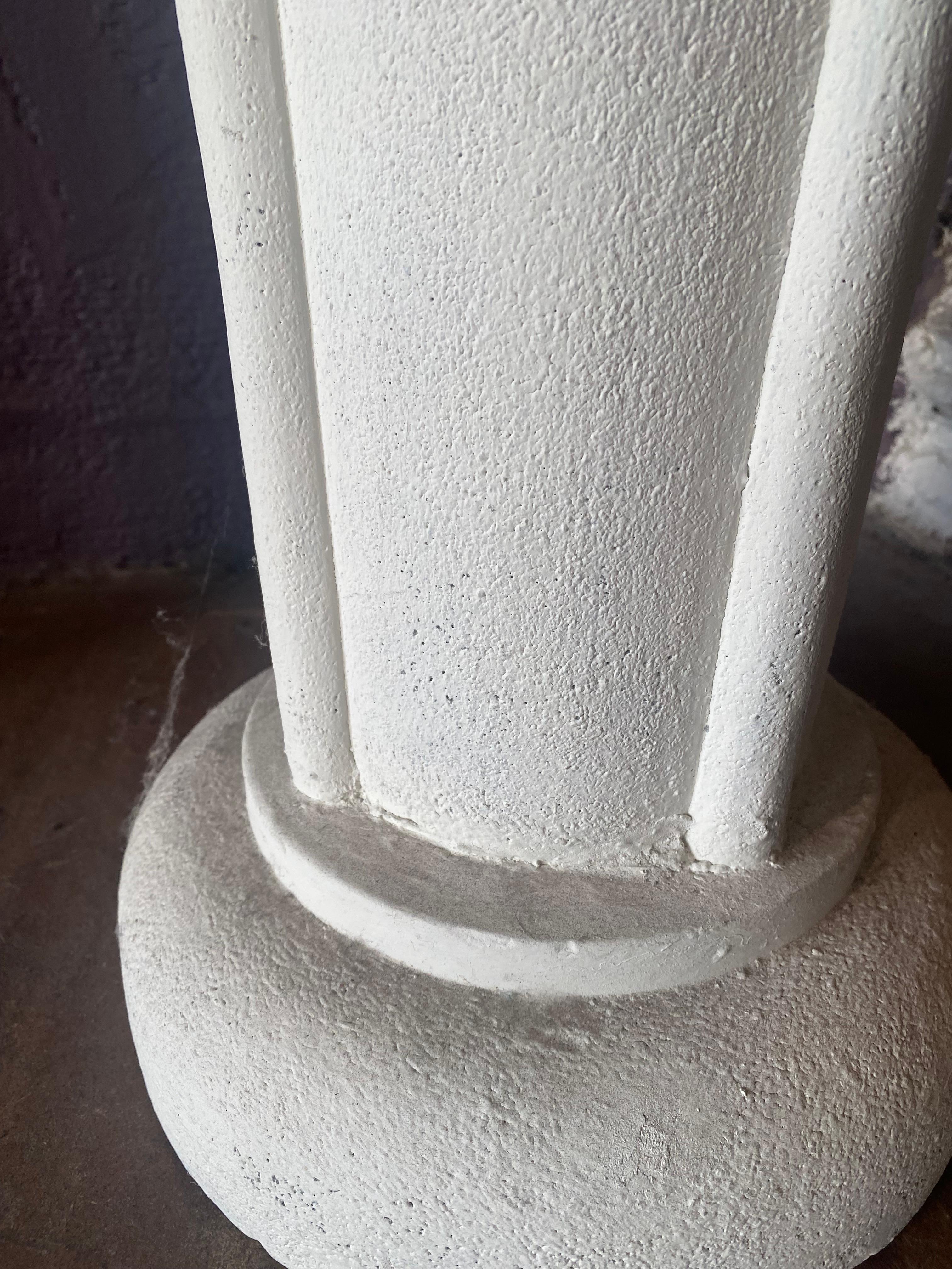 This contemporary pedestal reflects a blend of ancient and modern influences. Crafted from white plaster in the Greek Revival style, it features clean architectural lines and a subtle nod to classical design. The piece is distinguished by four