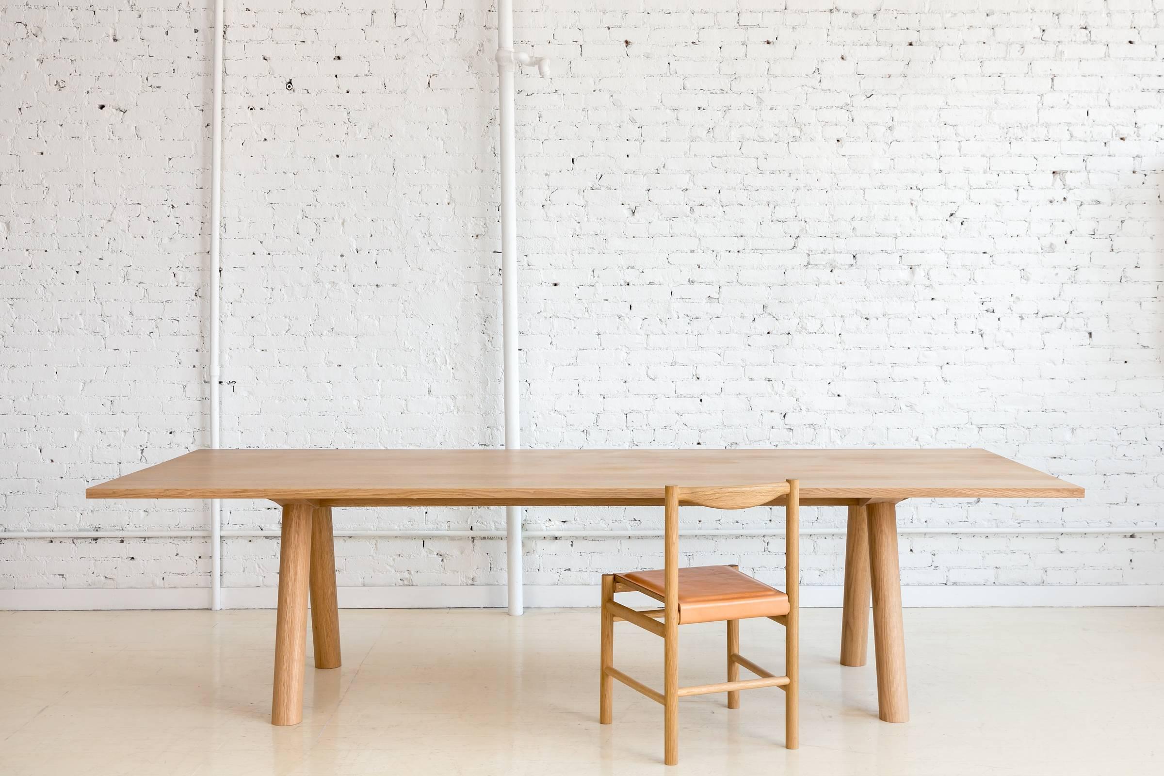 This contemporary, minimal dining table features large diameter wood legs and a bold trestle to give rise to an elegant hardwood top. Top includes rounded corners with an optional underside bevel to compliment details found on the base.

Made to