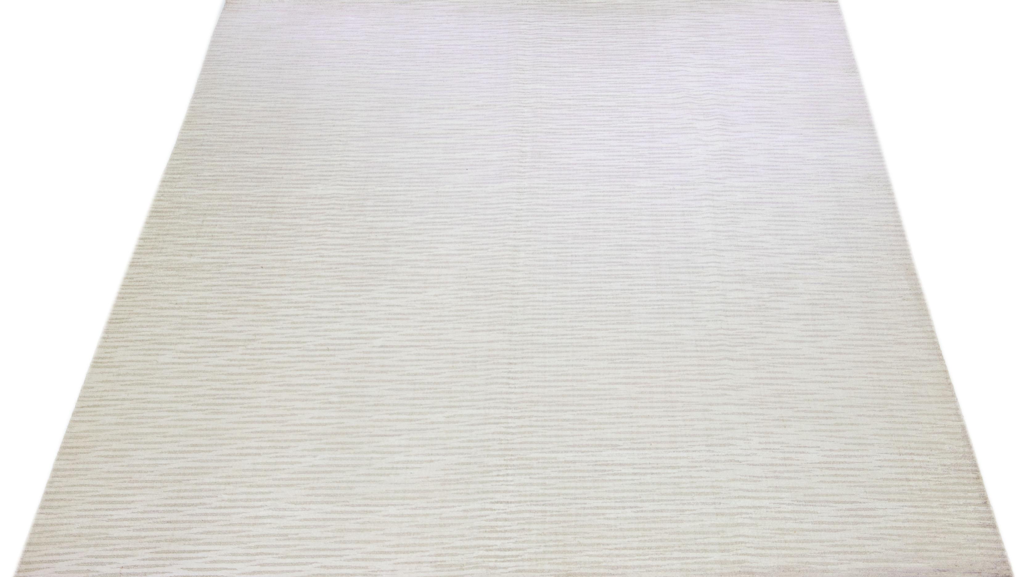 Cet exquis tapis contemporain en laine et soie présente une base gris-argent frappante ornée d'un étonnant motif géométrique qui s'étend gracieusement d'un bout à l'autre.

Ce tapis mesure 10' x 13'9