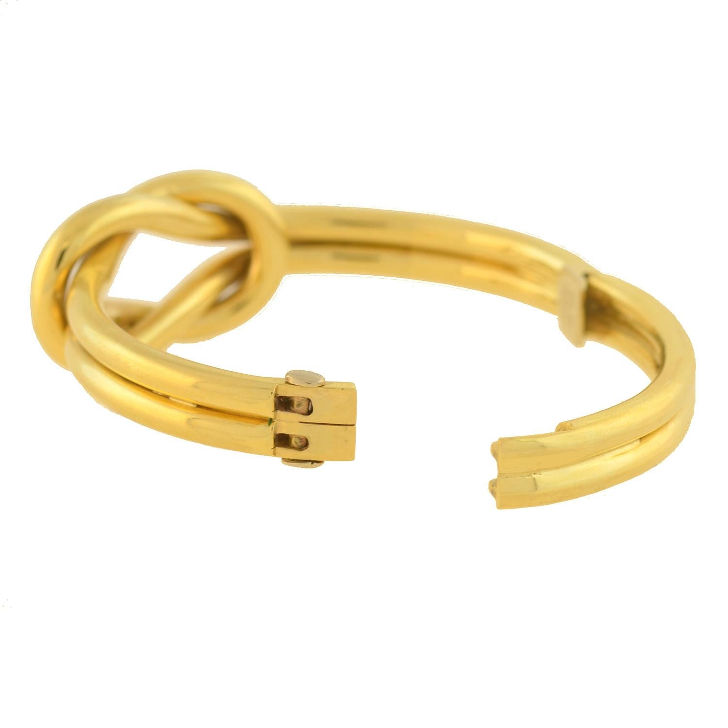 A stunning Estate love knot bangle bracelet from 1970s era! Crafted in 18kt yellow gold, this gorgeous piece features a large love knot design at its center. The bangle is comprised of two gold tubes that wrap around the wrist and intertwine at the