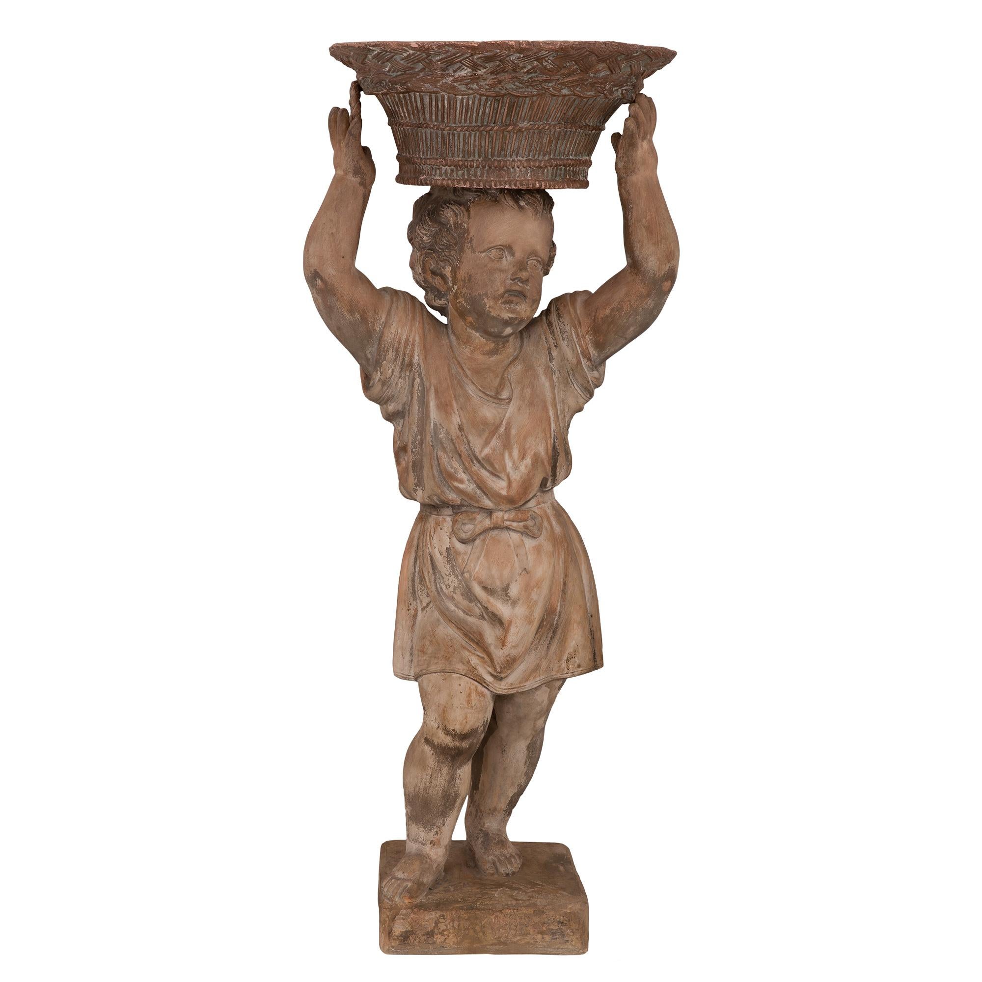 A charming Continental 18th century terra cotta statue/planter of a young boy. The statue is raised on a square terra cotta base. Above, the young boy stands dressed in a flowing tunic tied at the waist with a ribbon. He stands with his arms raised