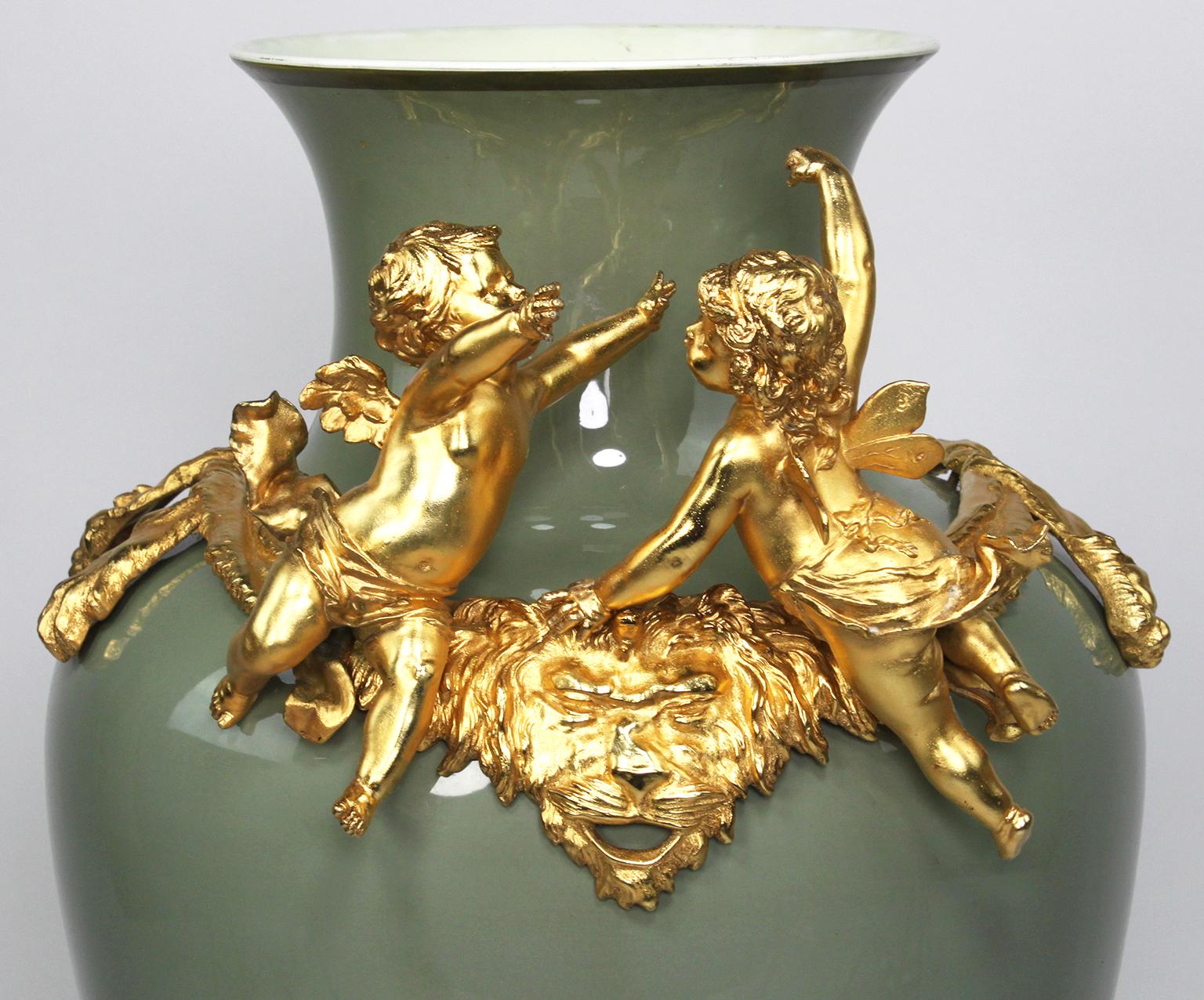 A continental 19th-20th century Romantic style porcelain and gilt metal mounted figural vase, probably French. The ovoid artichoke green porcelain body surmounted with a pair of hovering cherubs over a lion pelt, raised on scrolled feet. The