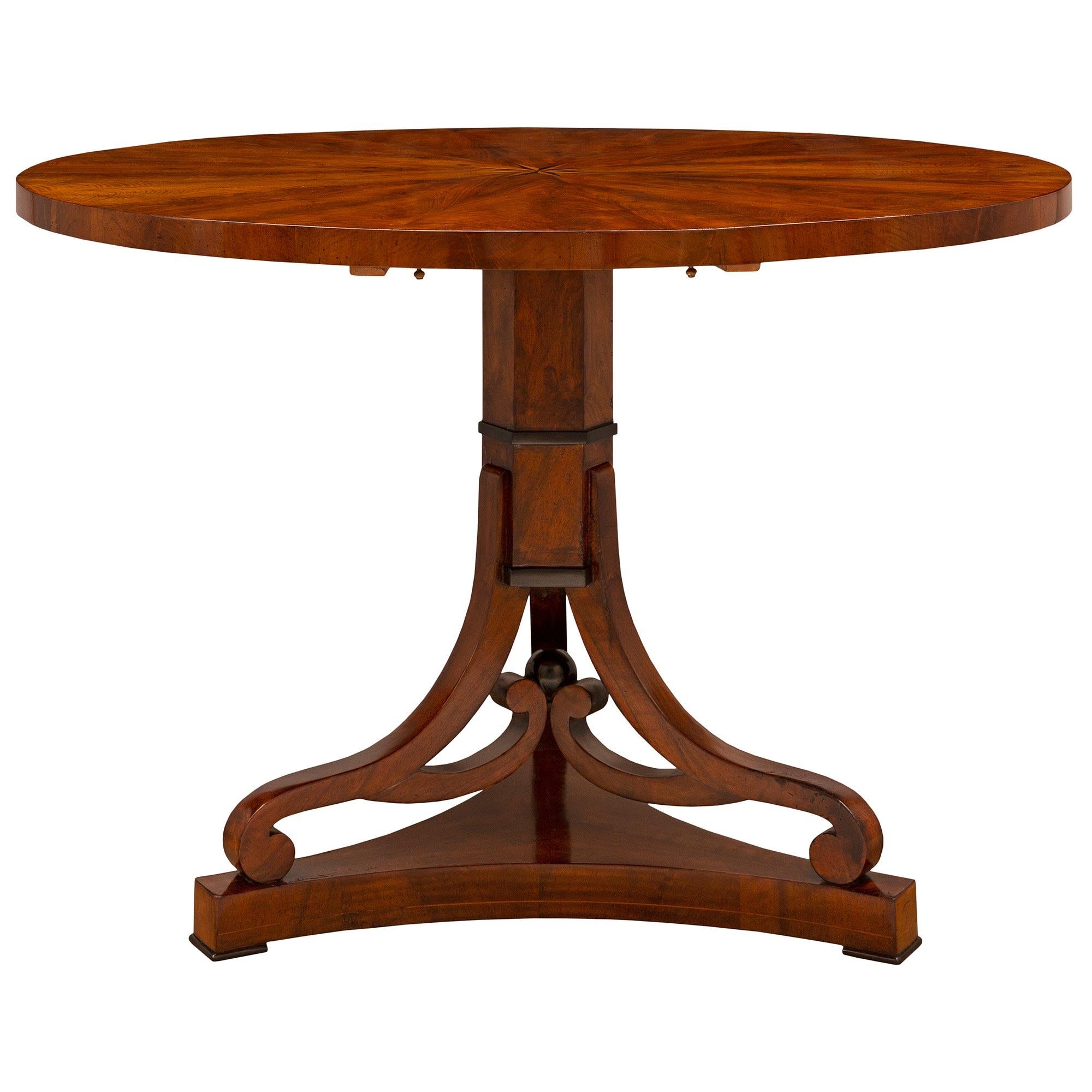 A handsome and most decorative Continental early 19th century Biedermeier st. flamed Mahogany, Fruitwood, and ebonized Fruitwood tilt top center/dining table. The circular table is raised by a beautiful triangular base with fine feet, concave sides,