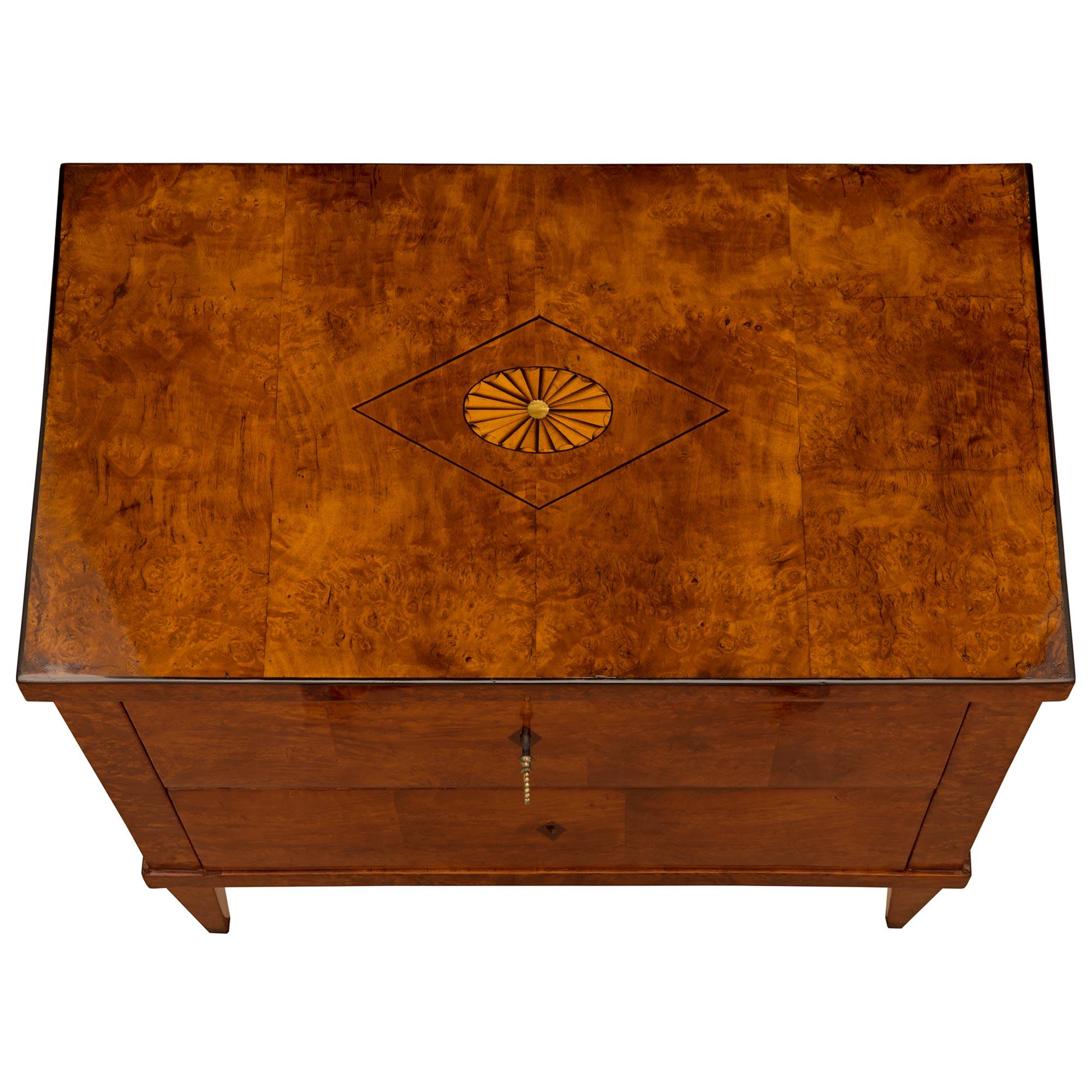 An outstanding Continental 19th century Biedermeier st. burl Walnut, ebonized Fruitwood, and mother of pearl commode. The two drawer chest is raised by elegant square tapered legs below the straight apron and two 'sans traverse' (without crossbar)