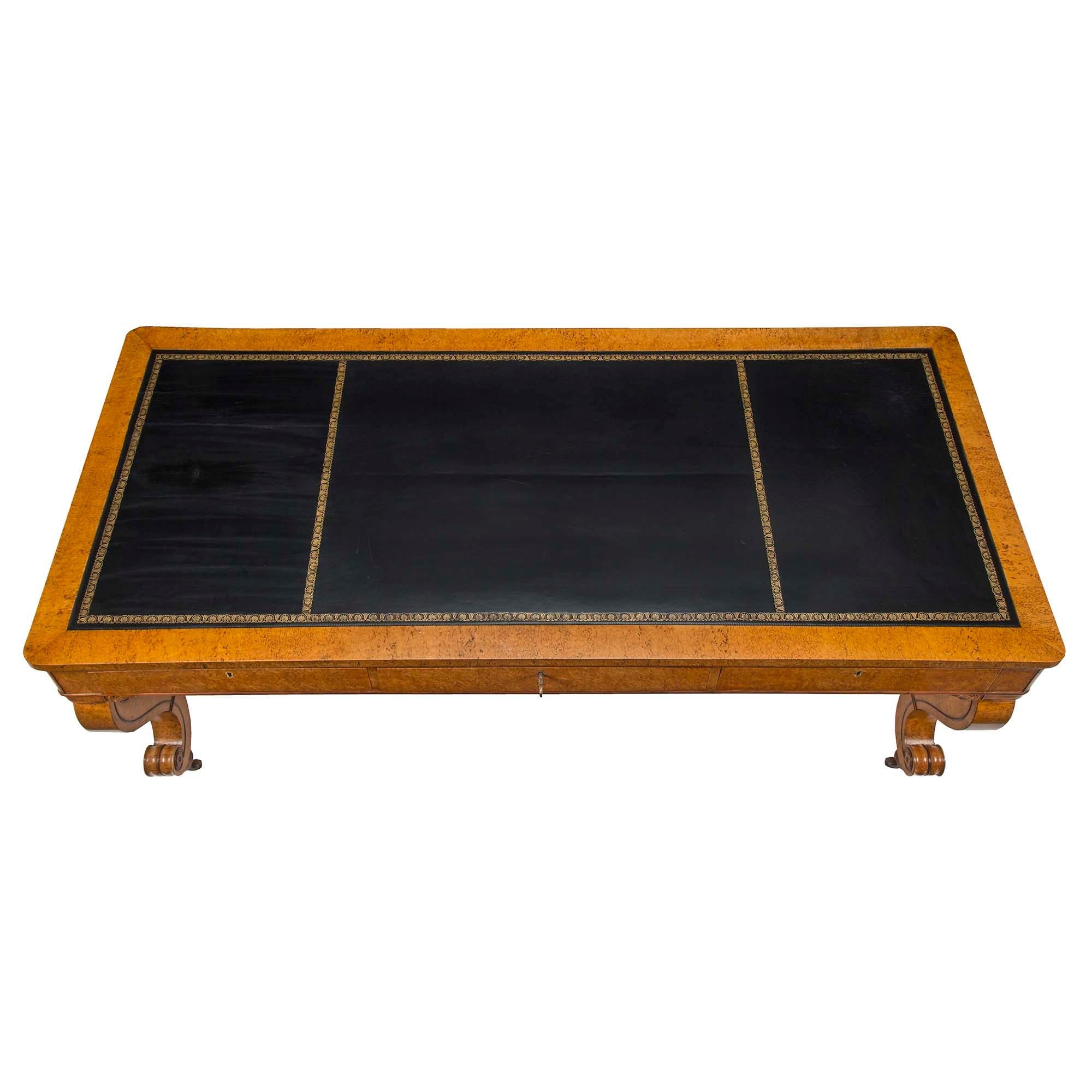 A stunning Continental 19th century Burl Maple Biedermeier center table/desk with ebonized fruitwood borders. Raised on brass casters are elegant scrolled legs rosette designs and scrolls joining them at each side. At the frieze are three wide
