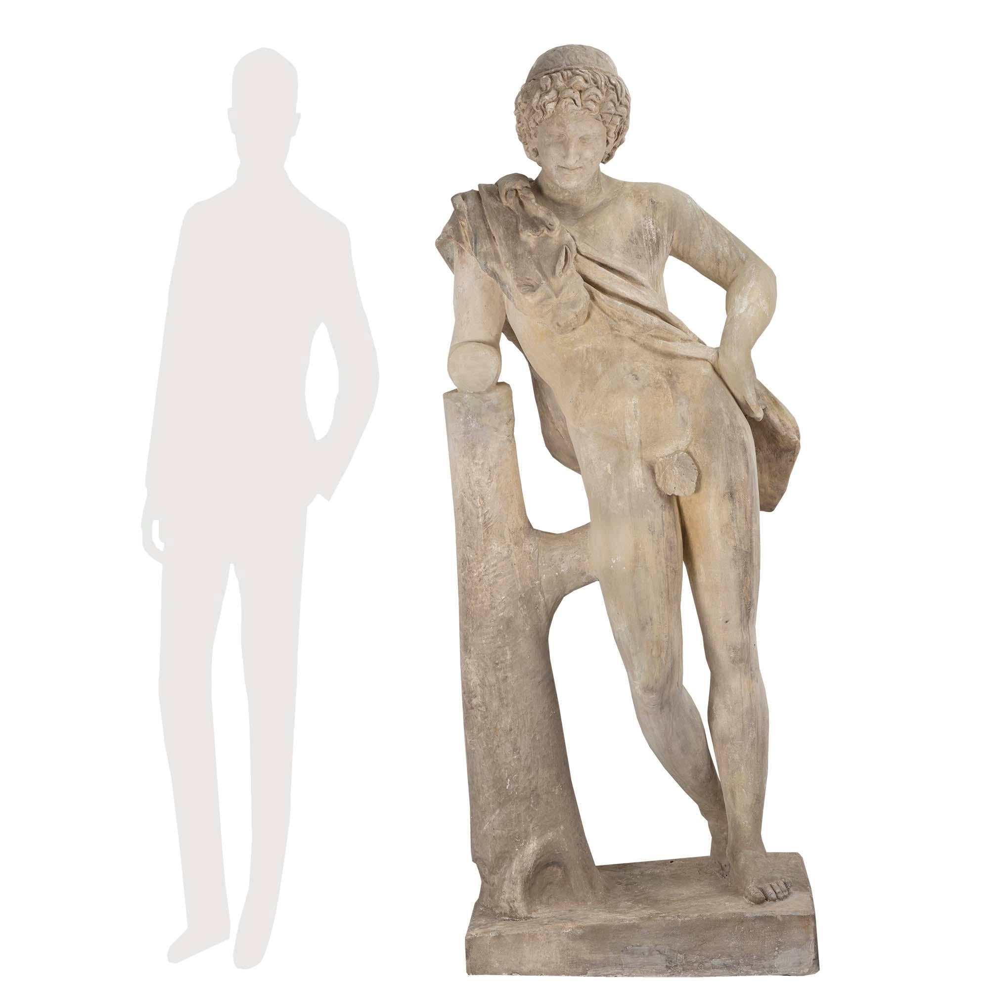 A handsome Continental 19th century plaster statue of a young hunter. The statue is raised on a rectangular base. The nude hunter is leaning on a tree trunk with his spoils draped across his shoulder and his left arm at his hip. Fine details and