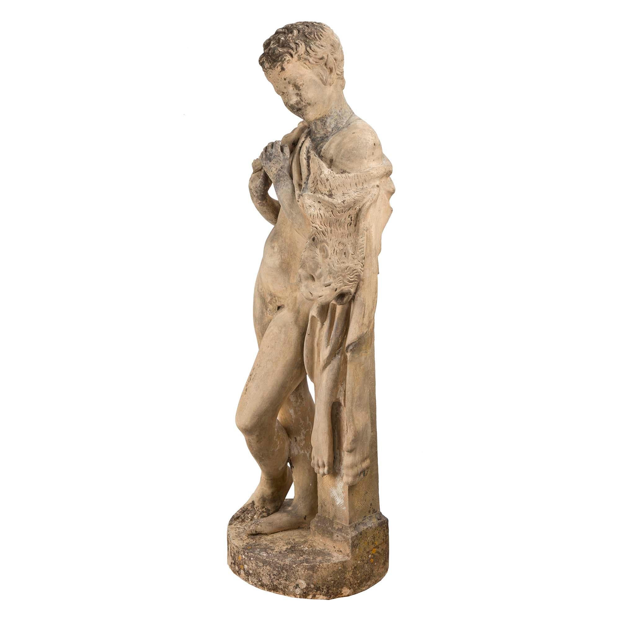 A most handsome and charming Continental 19th century terracotta statue of a young hunter. The young boy is standing on a circular base, leaning on a column. He is draped in his hunting spoils and is holding a flute. Rich wonderful details