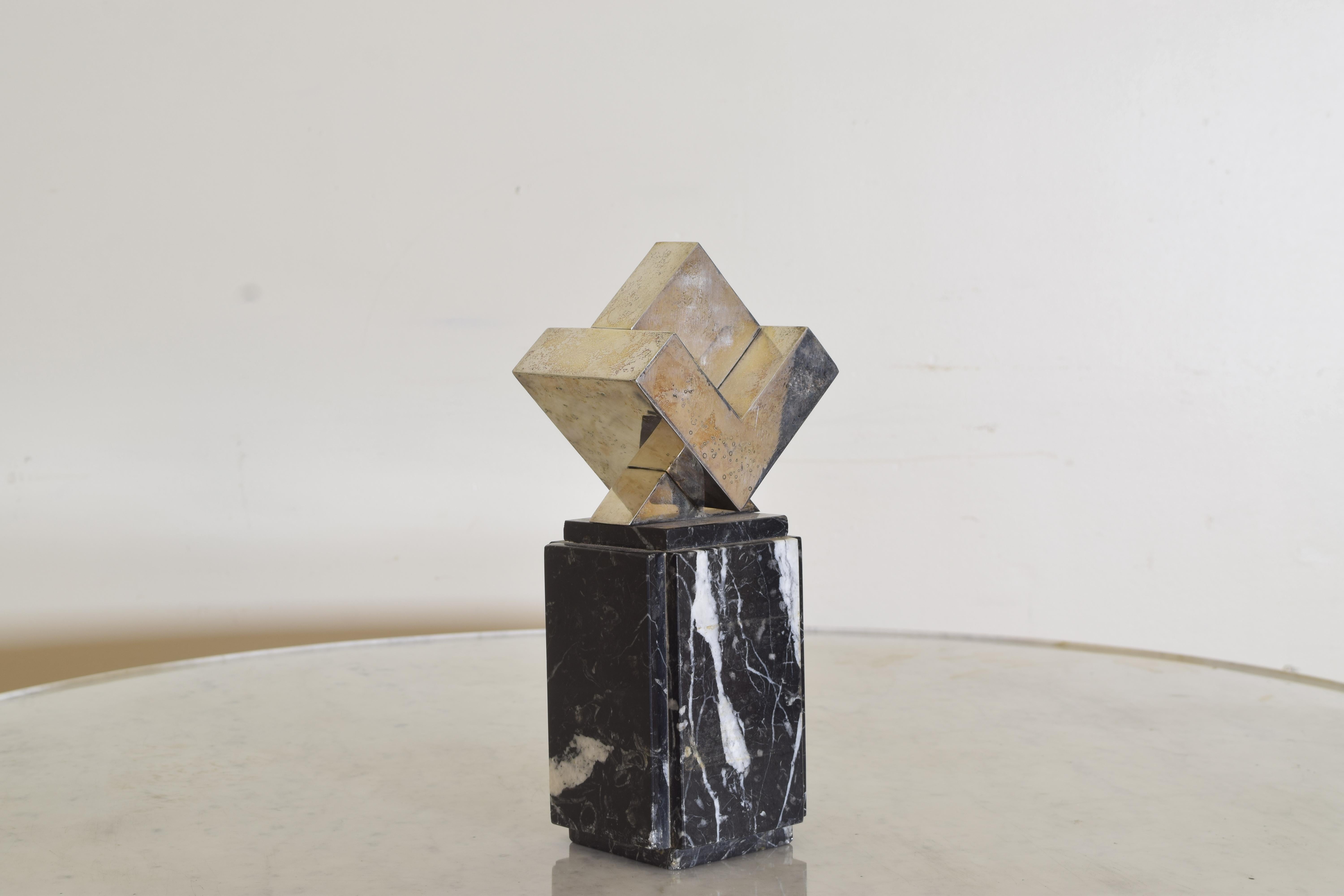 the sculpture is an abstract intertwined cube balancing on a corner mounted atop a marble stand.