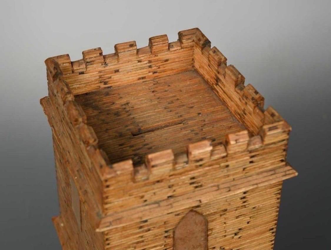 Une boîte à monnaie en allumettes d'art populaire, peut-être un prisonnier de guerre, 20e siècle, modelée comme une tour d'horloge avec une porte d'entrée et des fenêtres arquées et un sommet crénelé 21 cm de haut en très bon état sans dommages ou