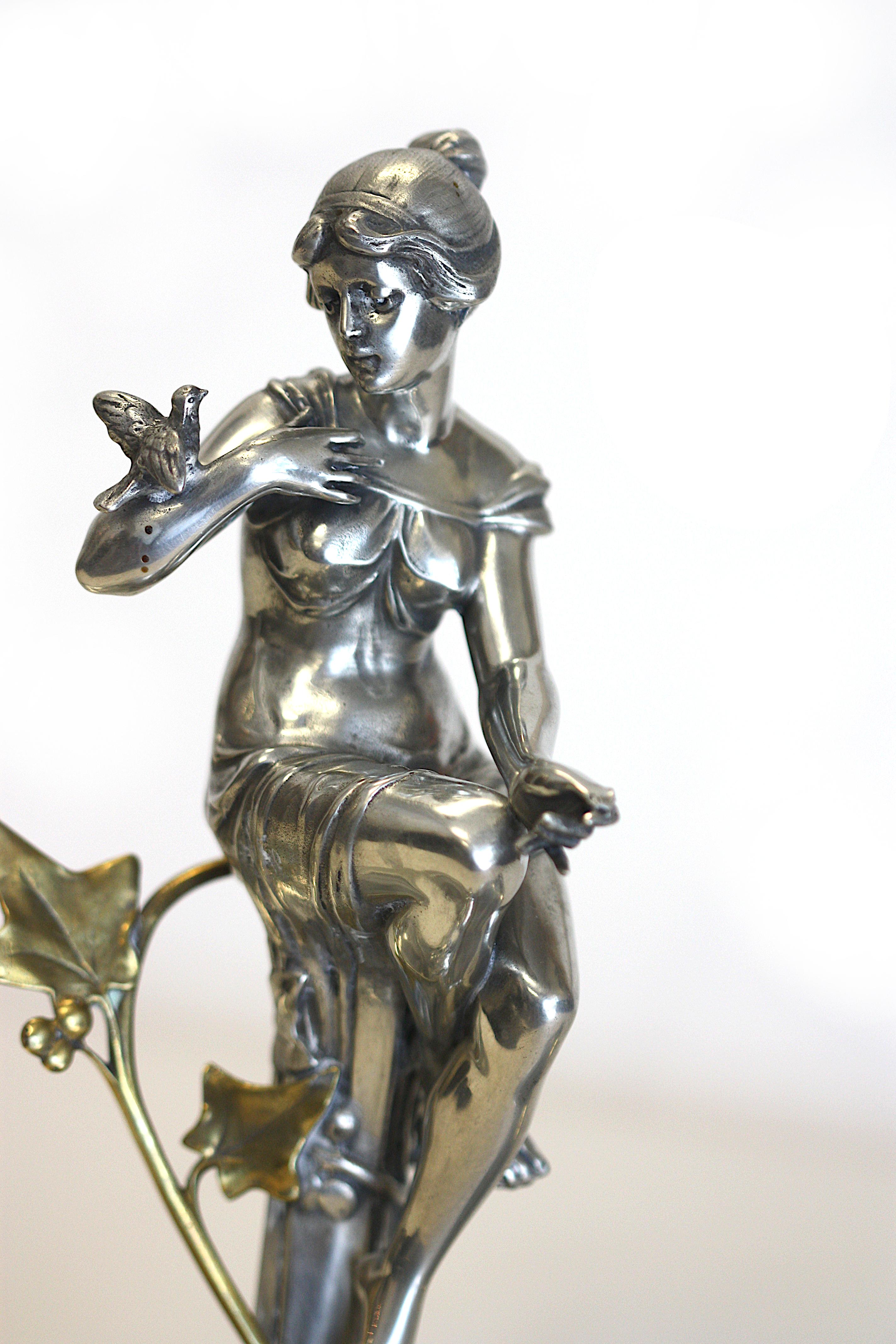 
Continental Art Nouveau Silvered Metal Centerpiece
Unmarked, probably WMF. The classically-clad maiden with a bird, atop a pedestal with a brass fitted berried twig, continuing to a double-dished platform with stylized twigs and open-scrolled ends.