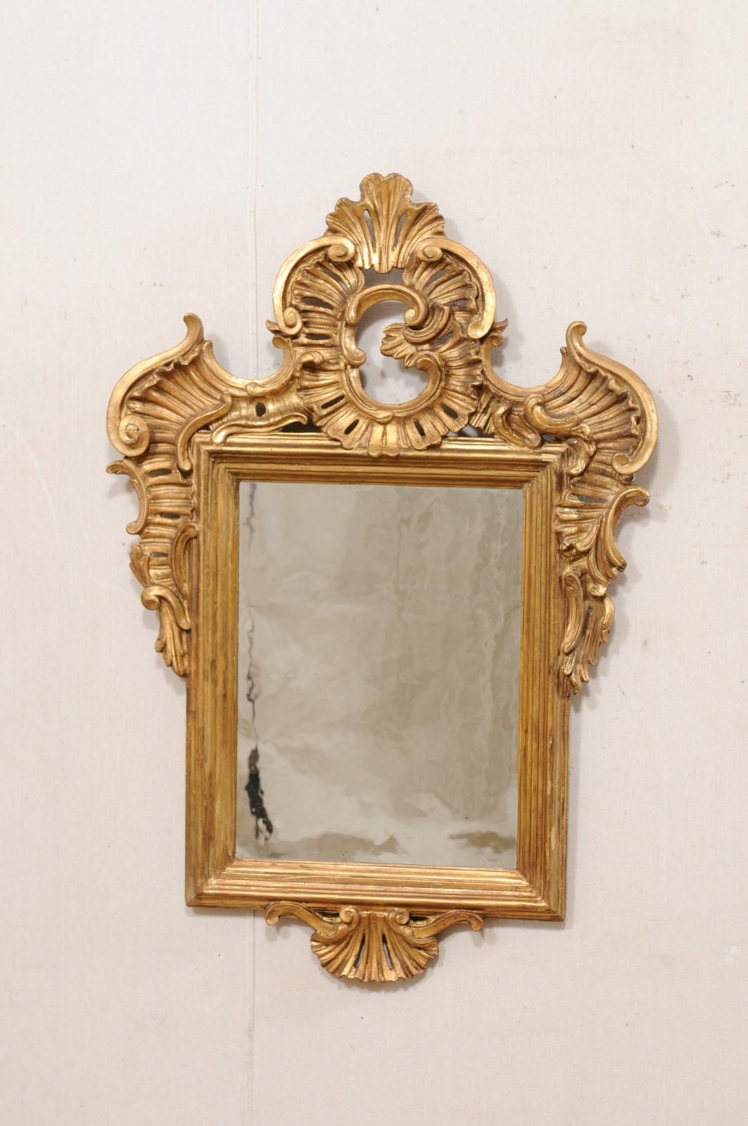 A Continental Baroque style wood carved and gilt mirror from the turn of the 18th and 19th century. This antique wall mirror from Europe has a rectangular-shaped mirror, with beautiful old wavy glass, set within a molded frame and elaborated adorn