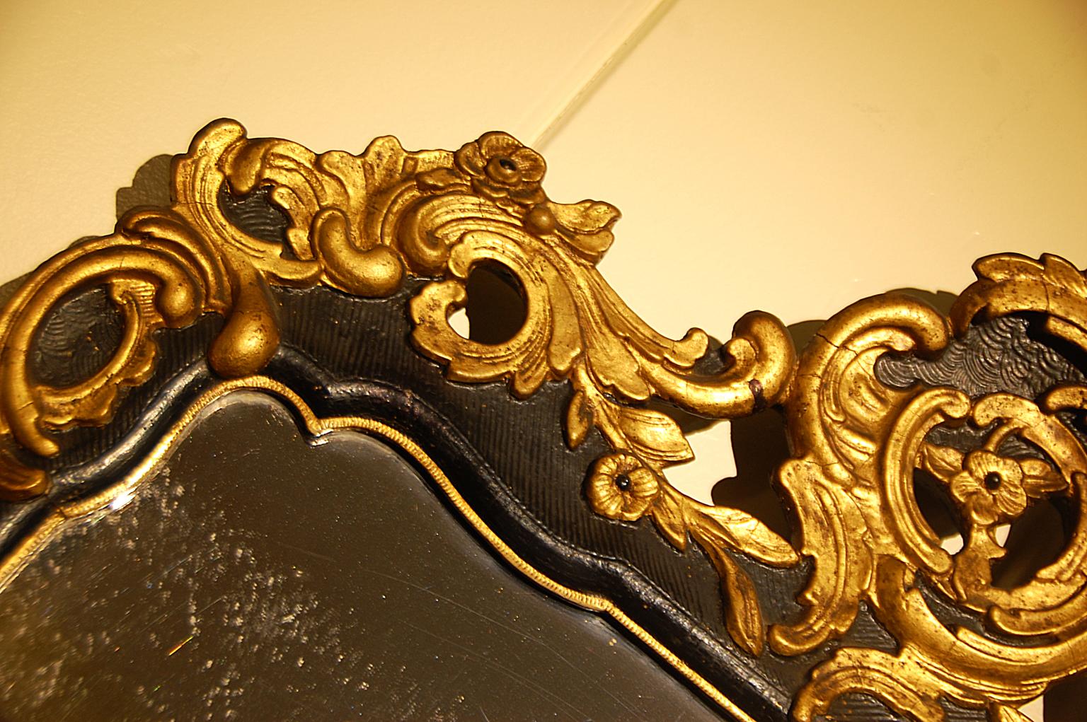 Continental hand carved late 18th-early 19th century parcel-gilt mirror. This elegant mirror has enhanced the leaf, shell and flower carvings by highlighting them in gold while keeping
the background simply shallowly carved and stained in black.