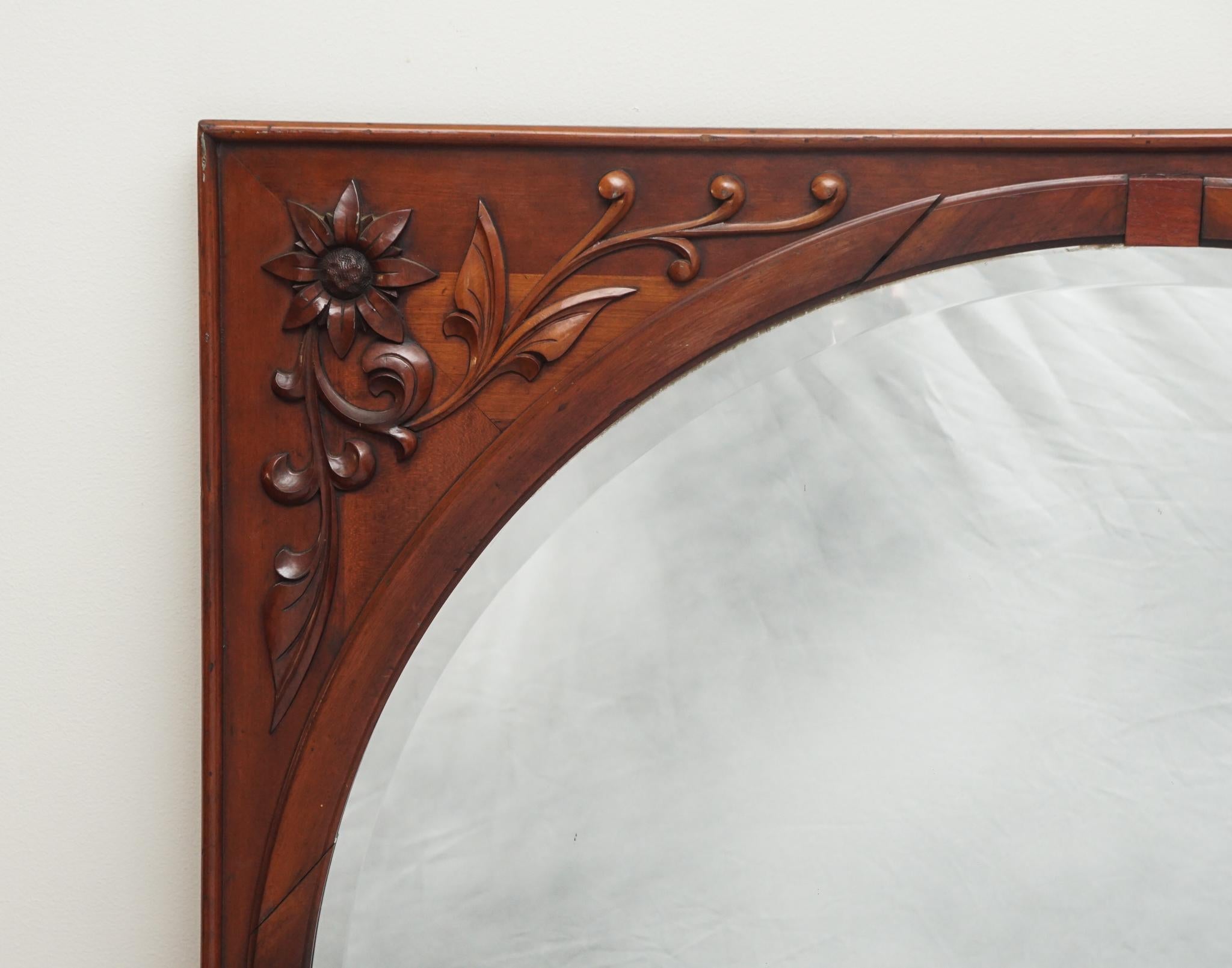 Questo squisito specchio in mogano intagliato. Caratterizzato da bellissimi fiori intagliati, la cornice in legno sovradimensionata circonda uno specchio smussato rotondo.  Alcuni piccoli segni di usura e separazione delle giunture, ma in generale