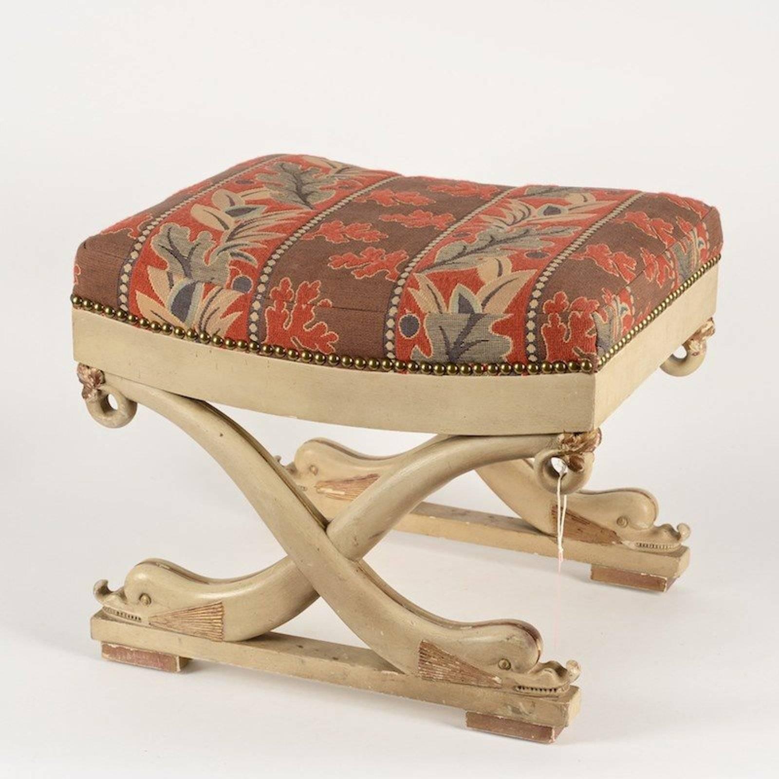 Late 19th century continental dolphin form stool in the Regency style; formed upholstered seat, painted and giltwood, nailhead trim.