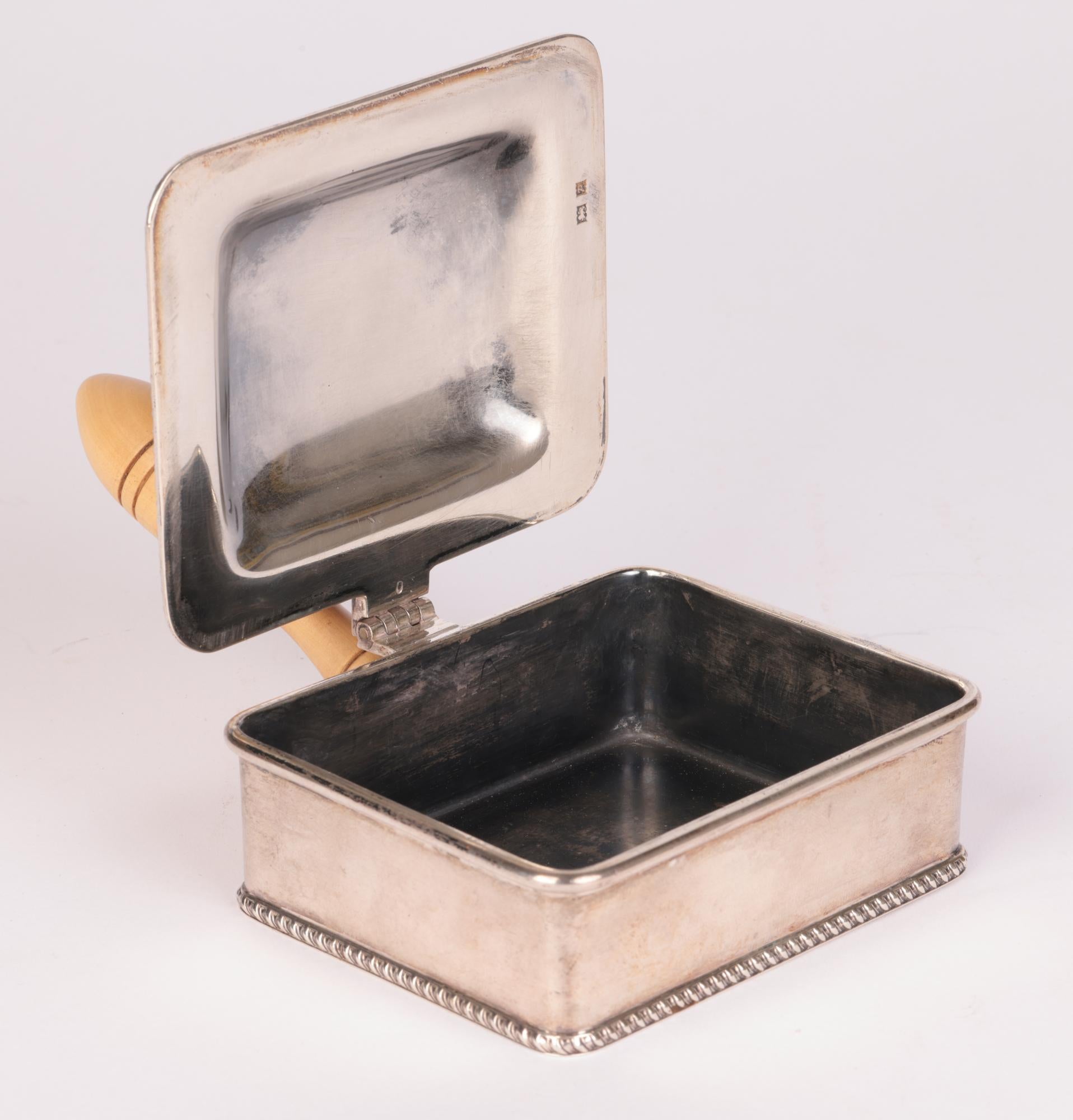 A stylish Continental, probably Dutch, wooden handled silver ashtray or cheroot holder dating from the 19th century. The heavily made container is of rectangular shape with hinged cover with a raised leaf thumb handle and small wooden turned handle.