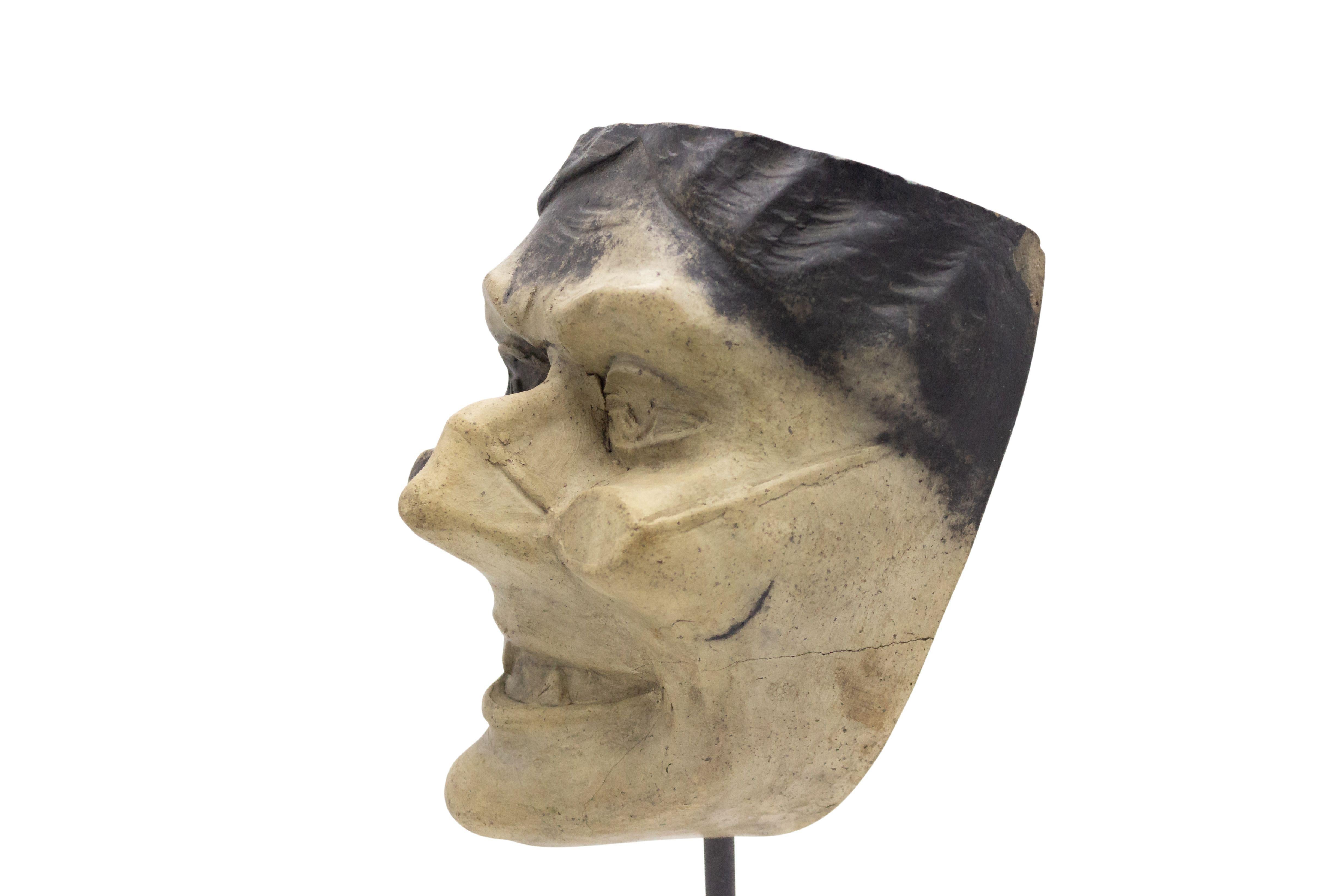 Continental German (late 19th cent) sculpted terra-cotta master mask mold of a laughing Grotesque face with glasses and pointed teeth displayed on a square black marble base stand (part of a 39 piece collection).
     