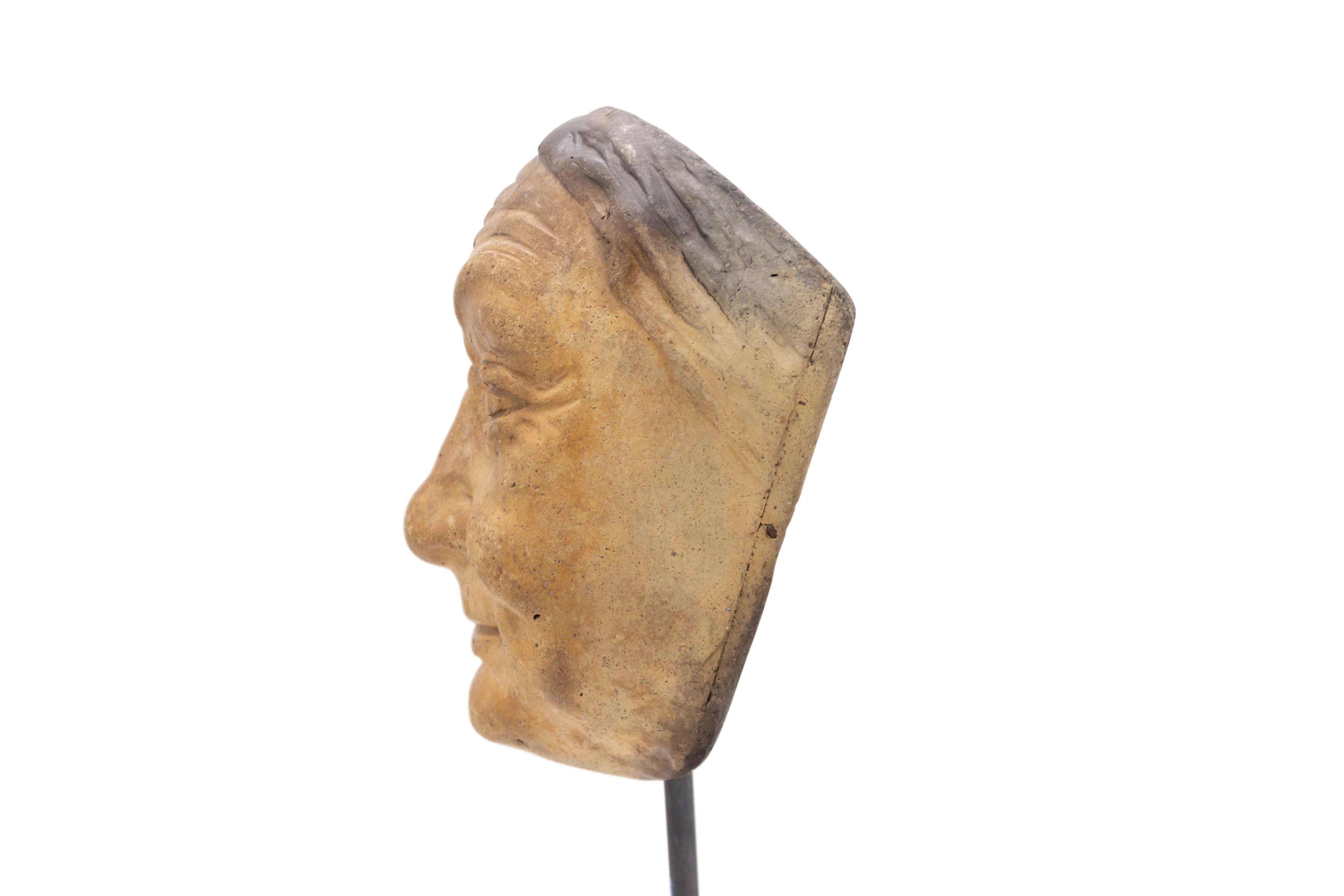 Continental German (late 19th cent) sculpted terra-cotta master mask mold of a smiling elderly face with hair parted in the middle displayed on a square black marble base stand (part of a collection).
       
