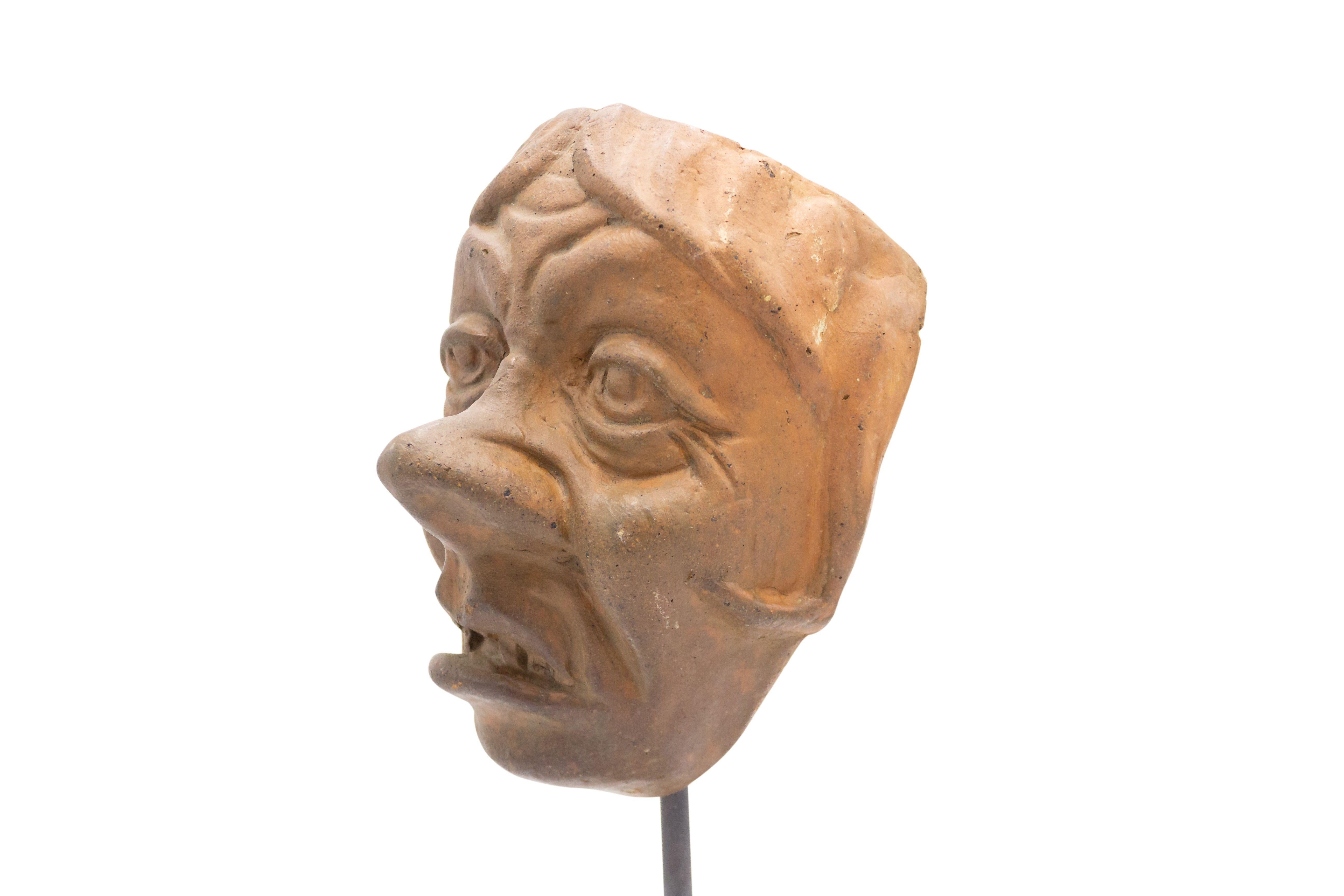 Continental German (late 19th cent) sculpted terra-cotta master mask mold of a sneering wrinkled face displayed on a square black marble base stand (part of a collection).
     