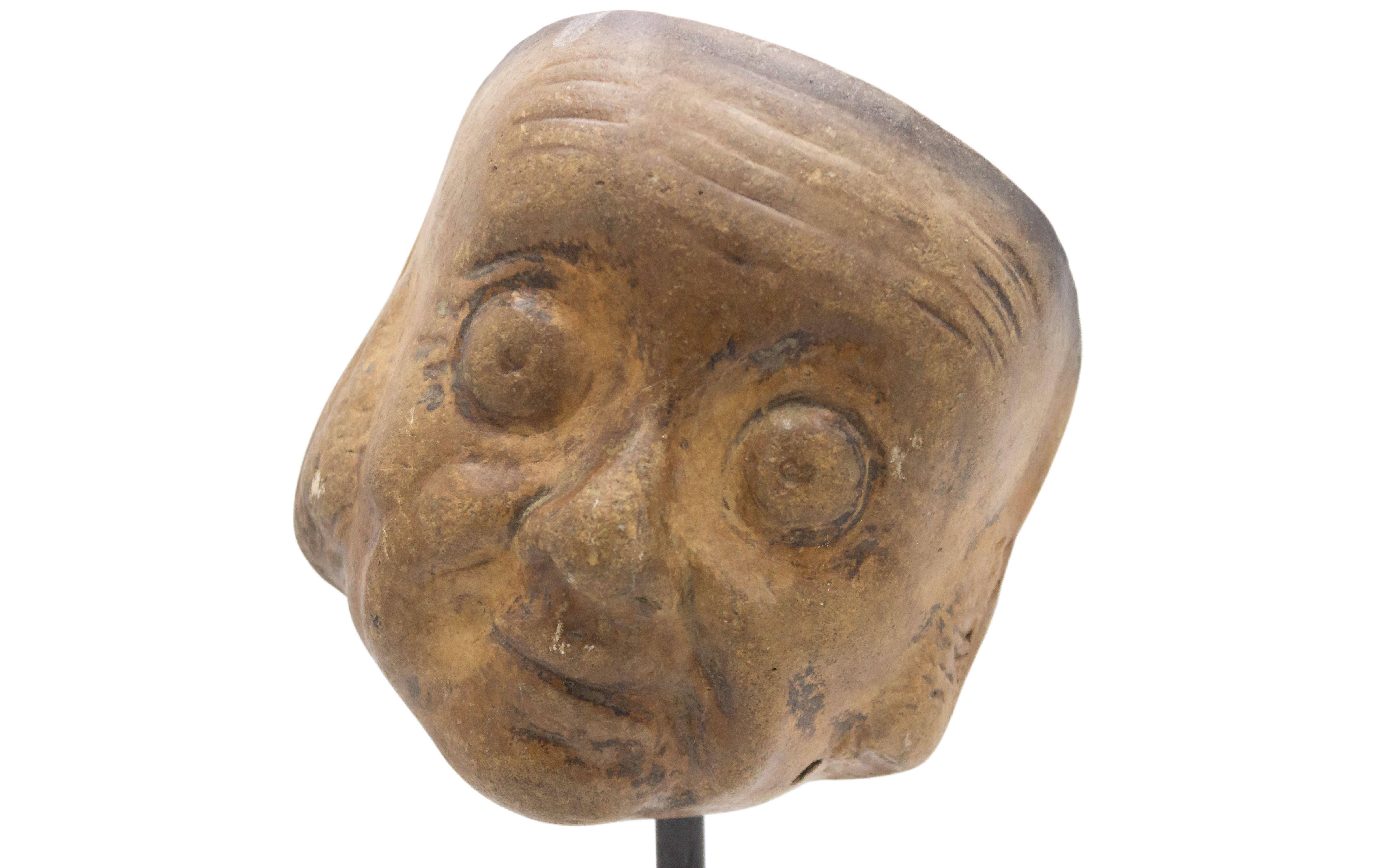 Continental German (late 19th Cent) sculpted terra-cotta master mask mold of a small google-eyed Grotesque face with a slight smile displayed on a square black marble base stand (part of a 39 piece collection).
 