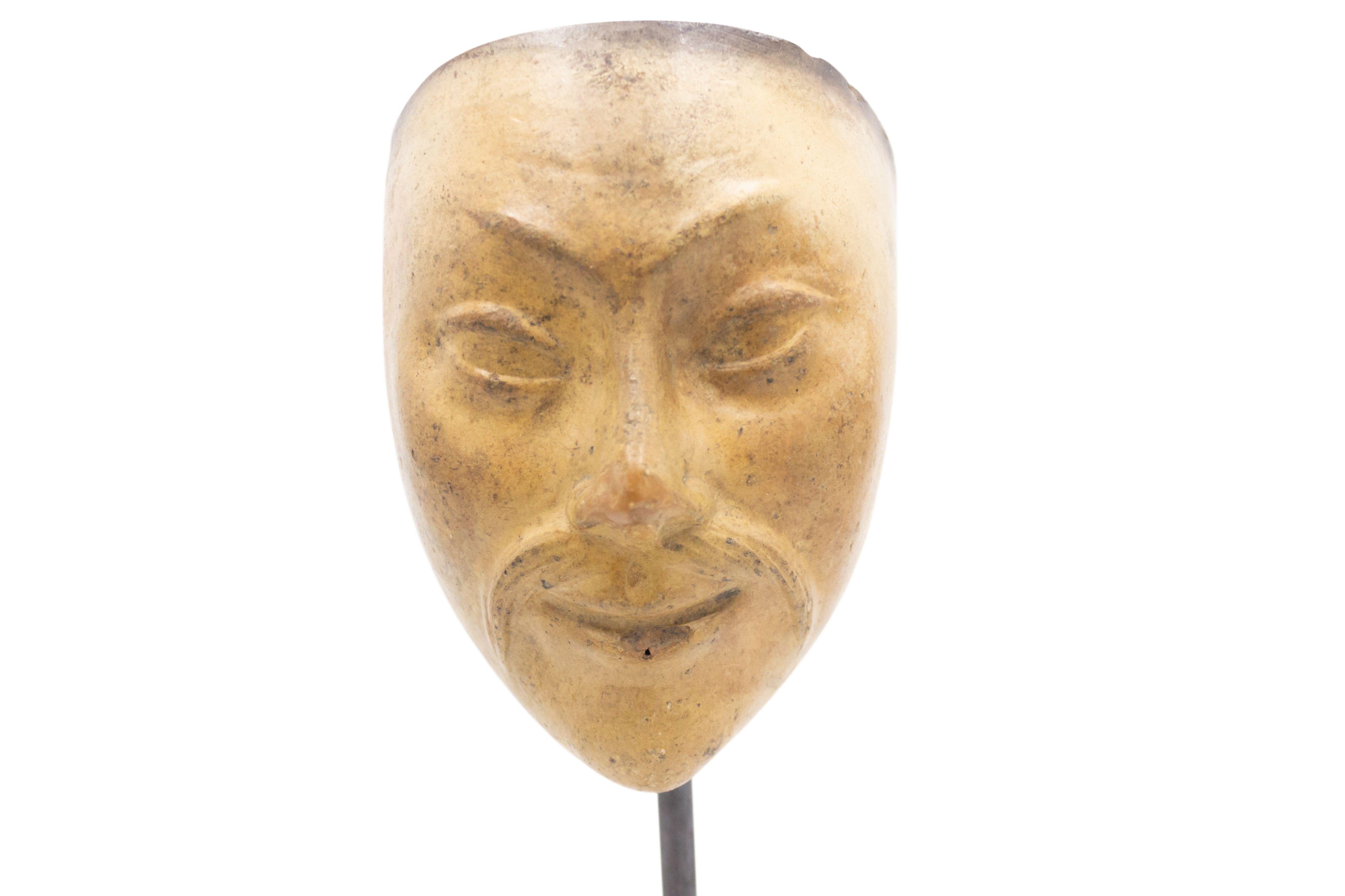 Maschera in terracotta scolpita di un piccolo volto asiatico con baffi e iniziali 