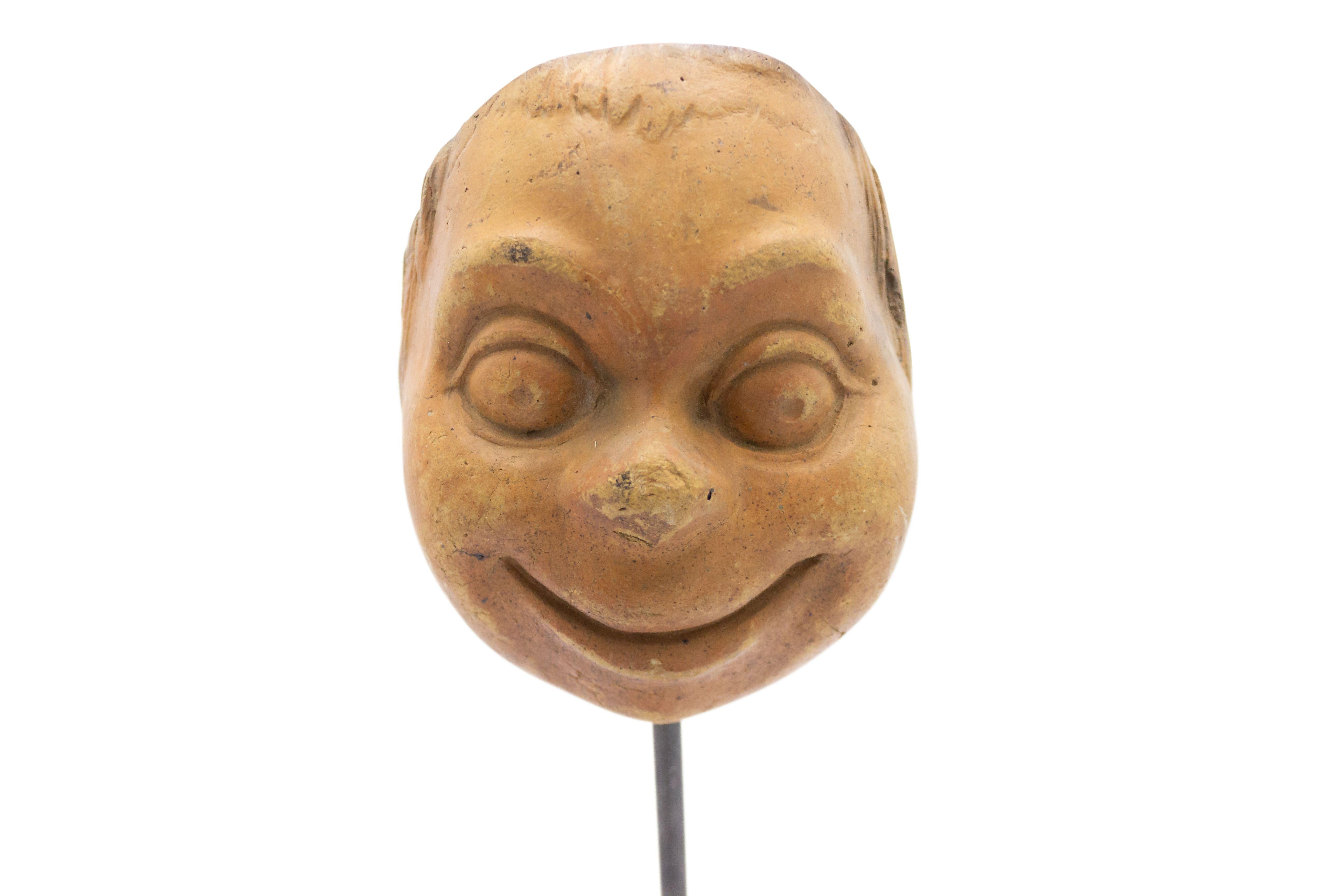 Continental German (late 19th Cent) sculpted terra-cotta master mask mold of a smiling google-eyed grotesque face displayed on a square black marble base stand (part of a collection).
 